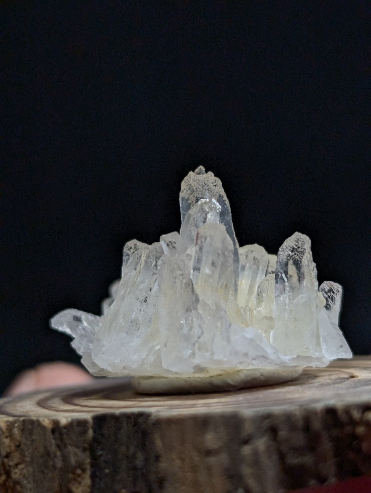 A translucent, pale quartz crystal cluster with jagged, pointed formations rests on a rustic wooden base.