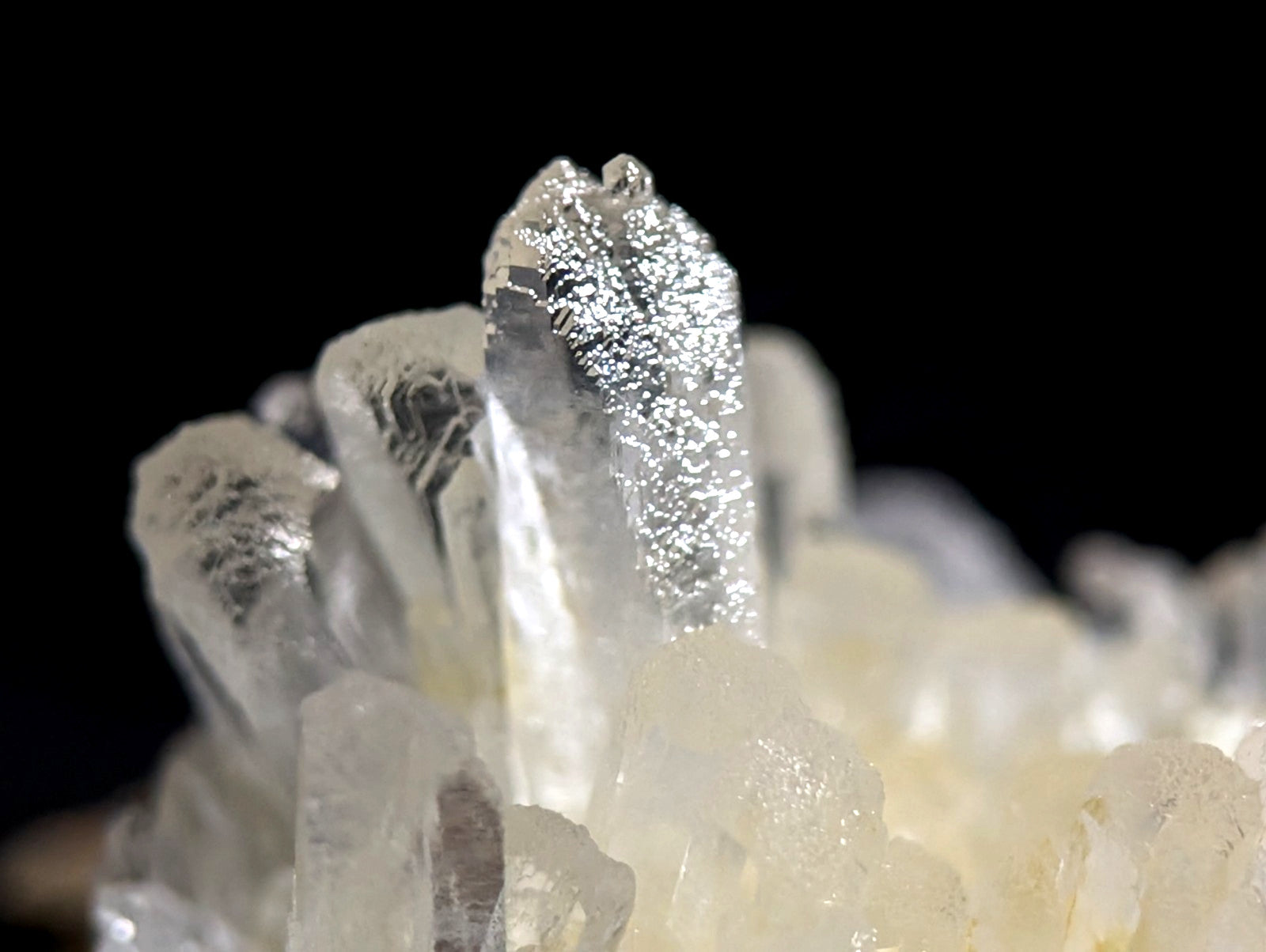 A translucent quartz crystal cluster with a central, elongated prismatic formation exhibiting subtle internal striations and a faintly metallic sheen.