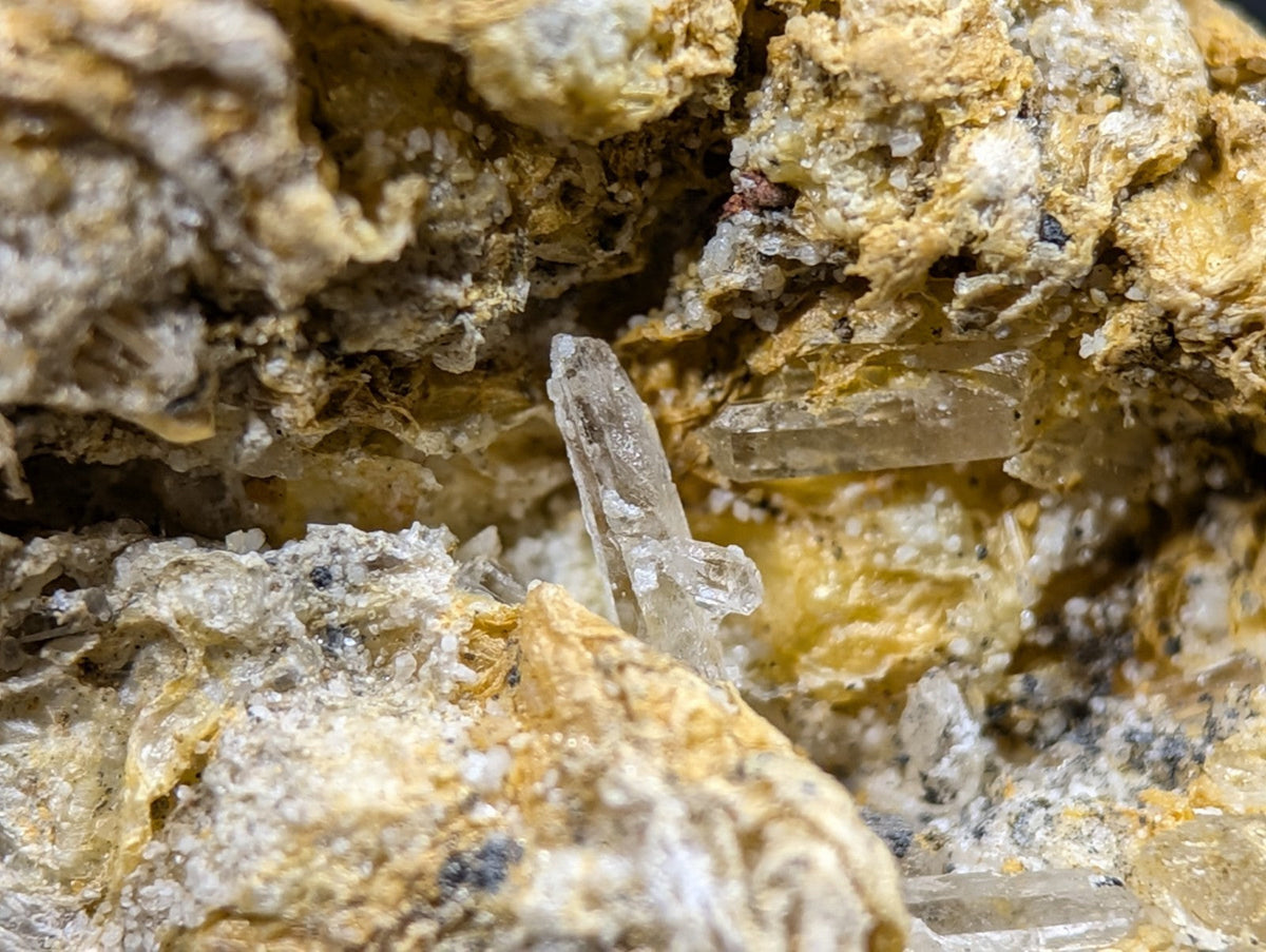 A translucent, crystalline mineral specimen with sharp facets and a pale, glassy sheen embedded within textured yellowish rock.