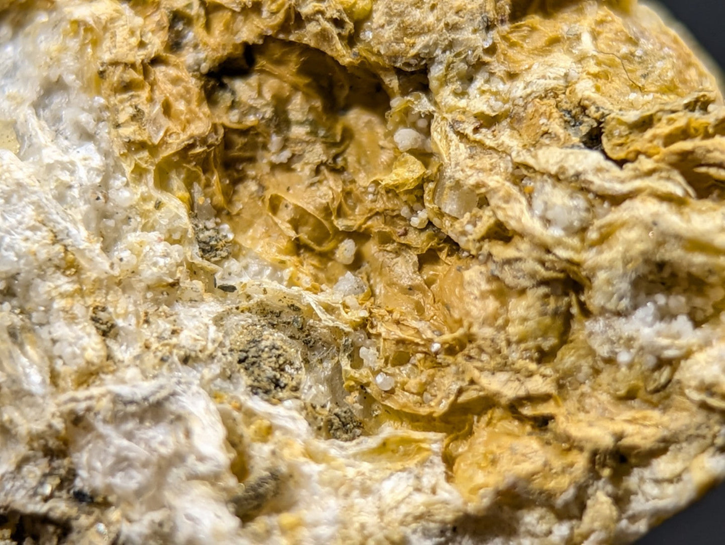 A textured, irregularly shaped mineral specimen with a mottled surface of yellowish-brown and white crystalline patches.