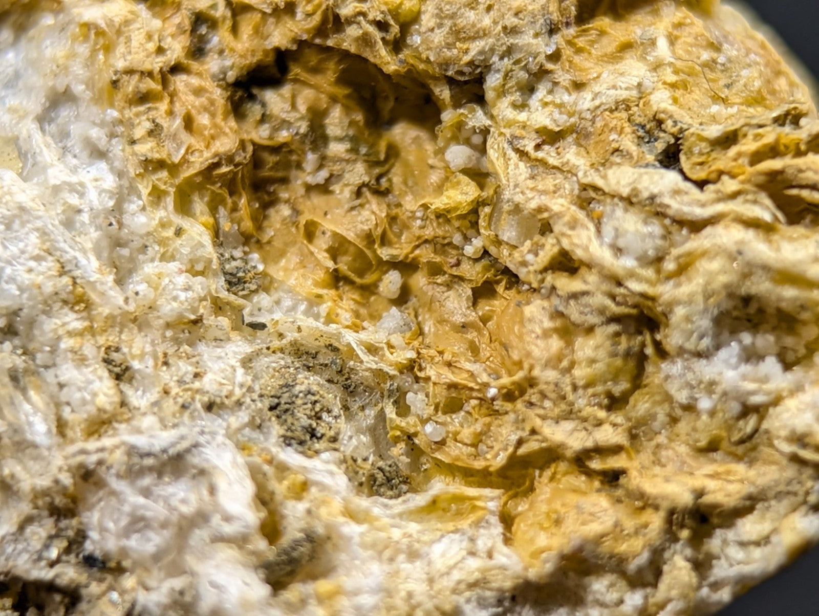 A textured, irregularly shaped mineral specimen with a mottled surface of yellowish-brown and white crystalline patches.