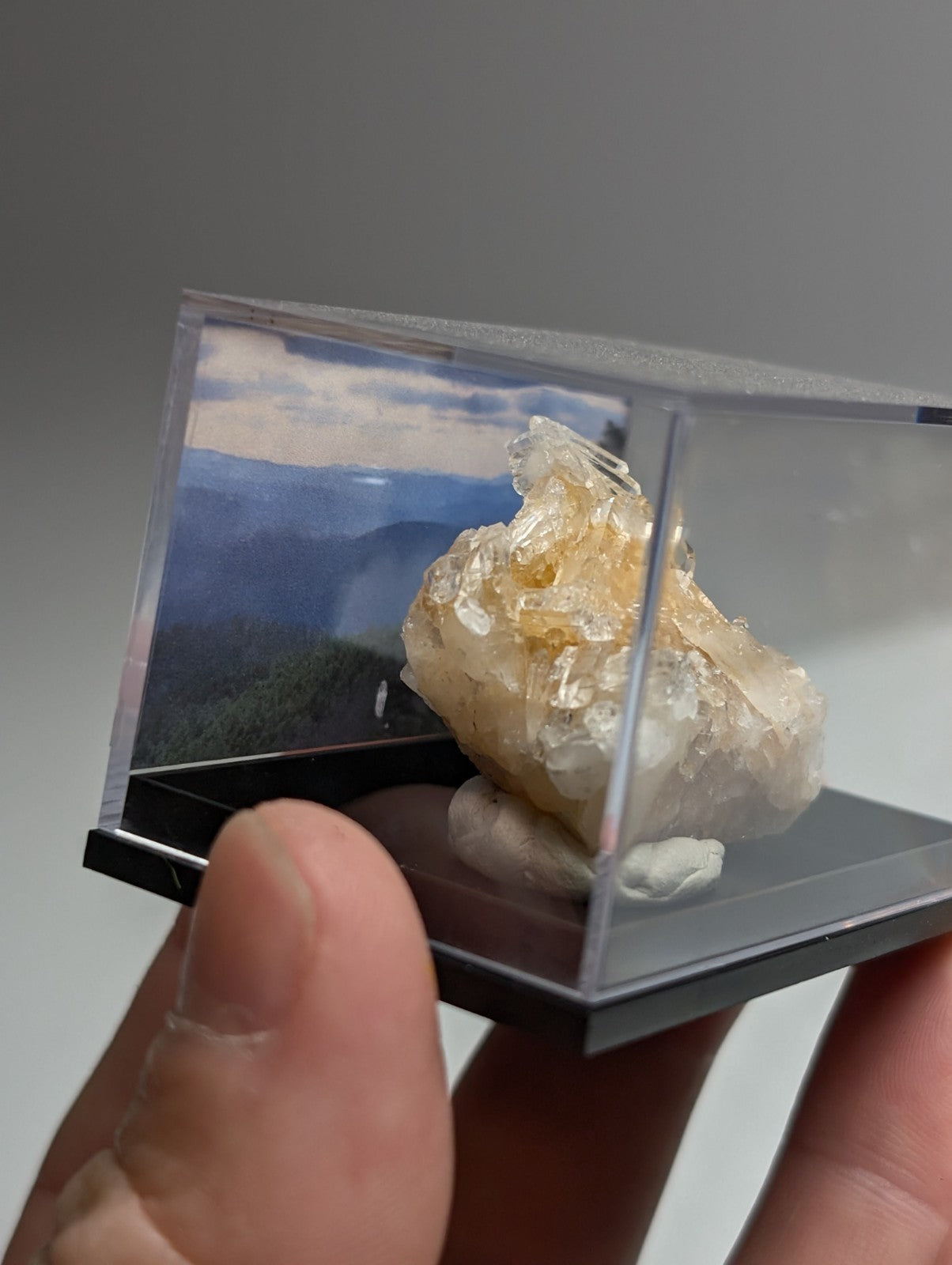 Solution quartz crystal cluster with translucent amber hue and rough texture displayed in clear acrylic case from saline county arkansas