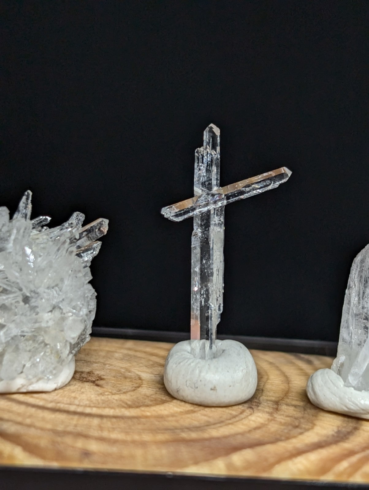 Clear quartz crystal cross mounted on a smooth, light gray stone base.