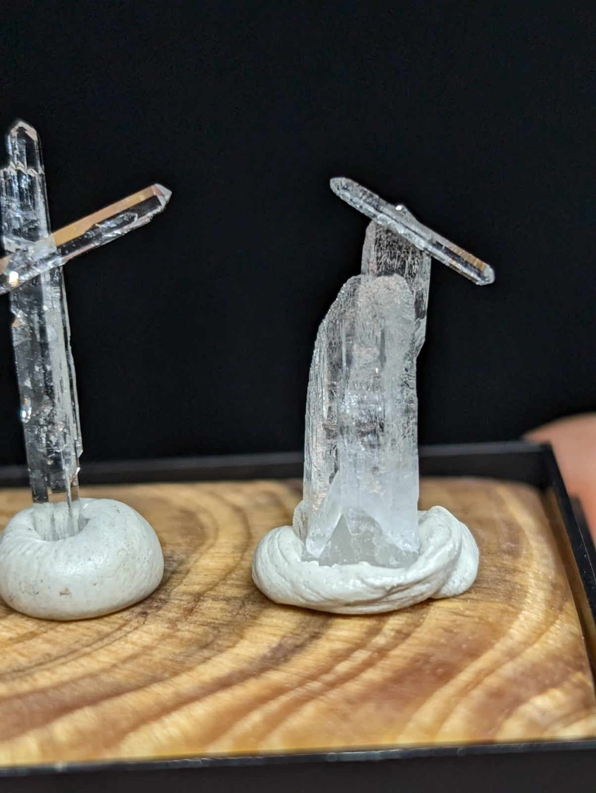 Two clear quartz crystal formations, each mounted on a white ceramic base and displayed on a wooden tray.