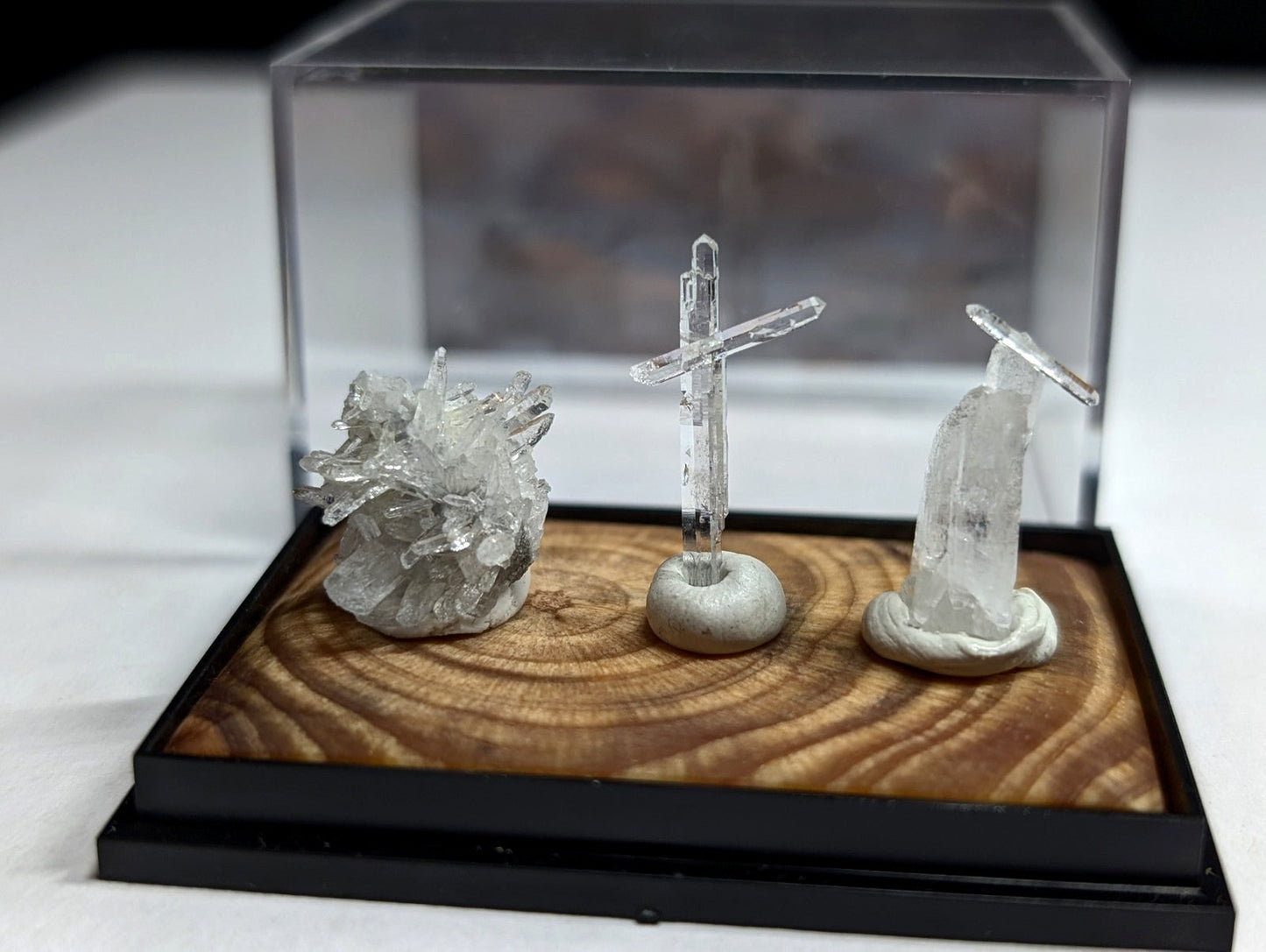 Clear quartz crystal formations displayed on a wooden base within an acrylic display case.