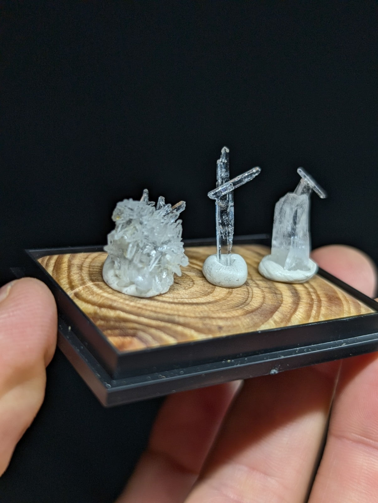 Miniature crystal display set featuring three translucent, clear quartz specimens mounted on a rustic wooden base with black frame.