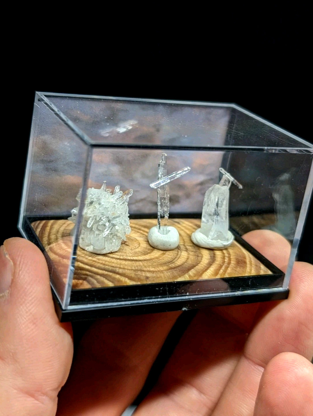 透明玻璃展示盒内盛放着三件微型水晶雕塑，包括一簇晶莹剔透的晶体、一个十字架造型和一座人物雕像。