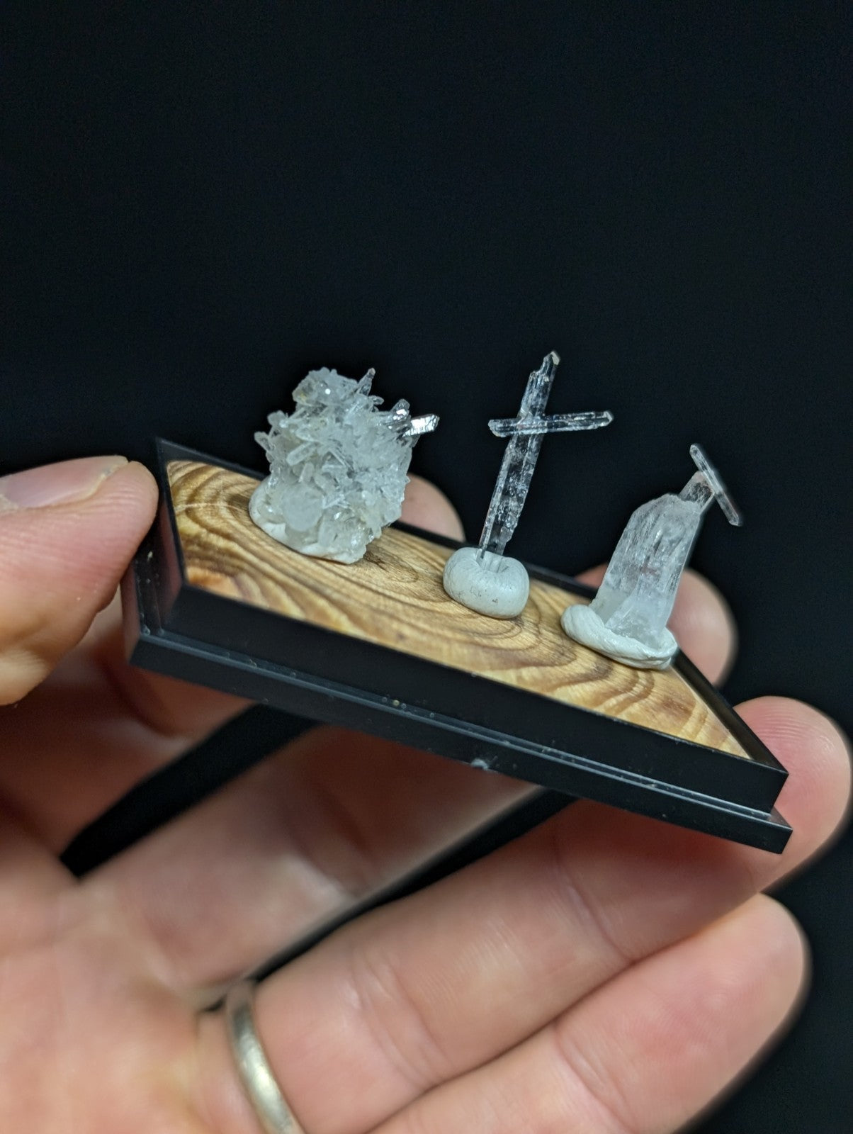 A miniature clear resin display featuring a crystal cluster, a cross, and a statue on a wooden base.