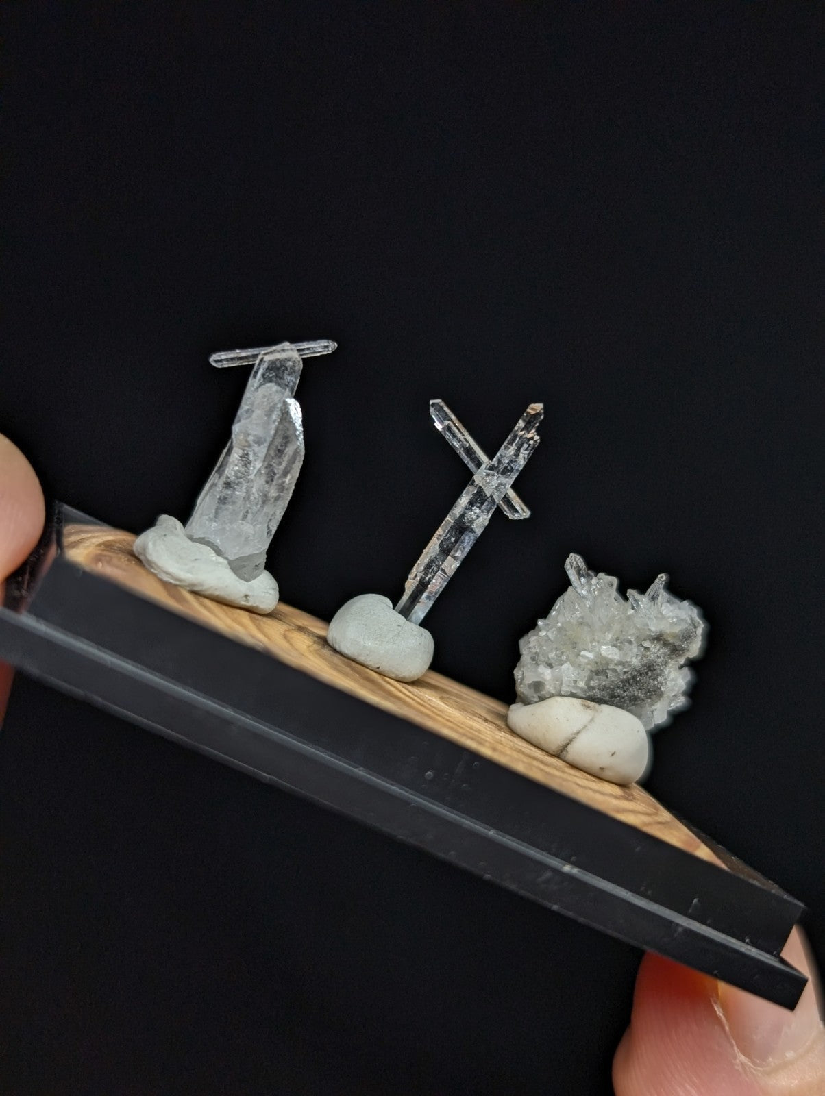 A clear quartz crystal display set featuring three distinct mineral specimens mounted on a wooden base with black trim.