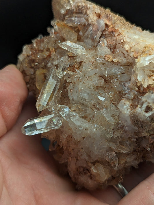 A cluster of clear, translucent quartz crystals growing from a rough, earthy brown matrix.