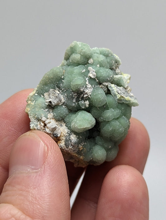 A cluster of light green, rounded mineral formations with a slightly rough texture and patches of white crystalline material.