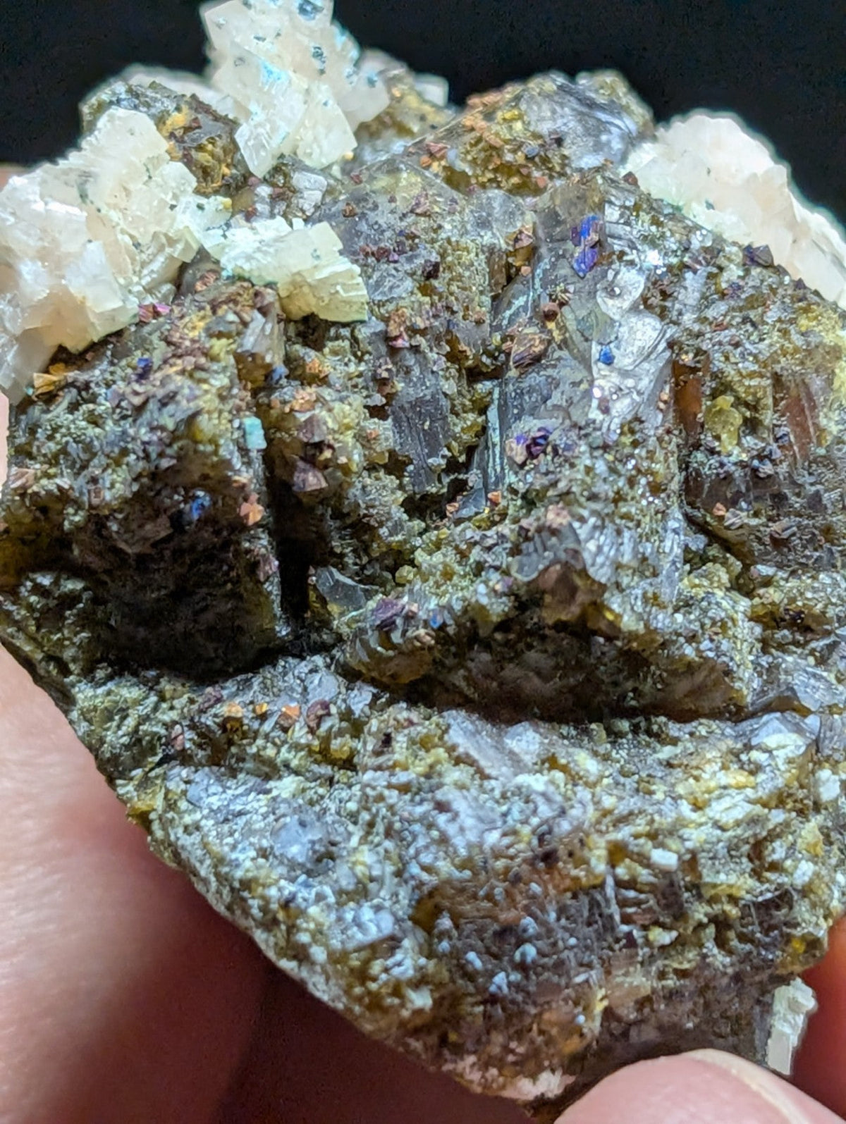 A rugged, earthy mineral specimen featuring translucent white crystals atop a dark, textured matrix with specks of purple and green.