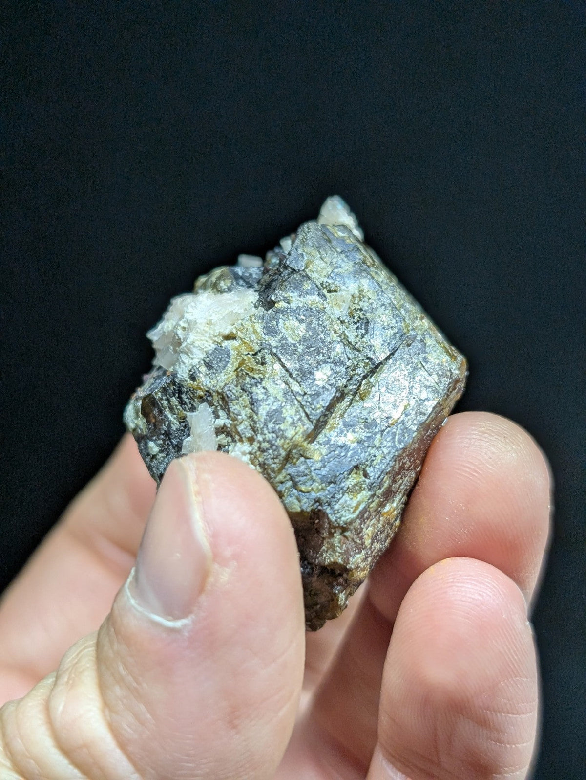A hand holds a rough, irregularly shaped mineral specimen with a mottled gray and white surface featuring visible crystalline formations.
