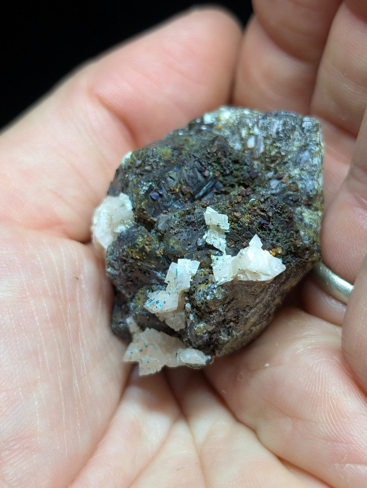 A dark, rough-textured mineral specimen with prominent white crystalline formations and subtle blue-green flecks.
