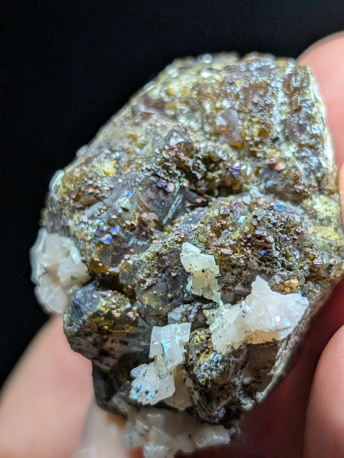 A rugged, irregularly shaped mineral specimen featuring translucent white crystals embedded in a dark, earthy matrix with hints of gold and iridescent blue-purple flecks.