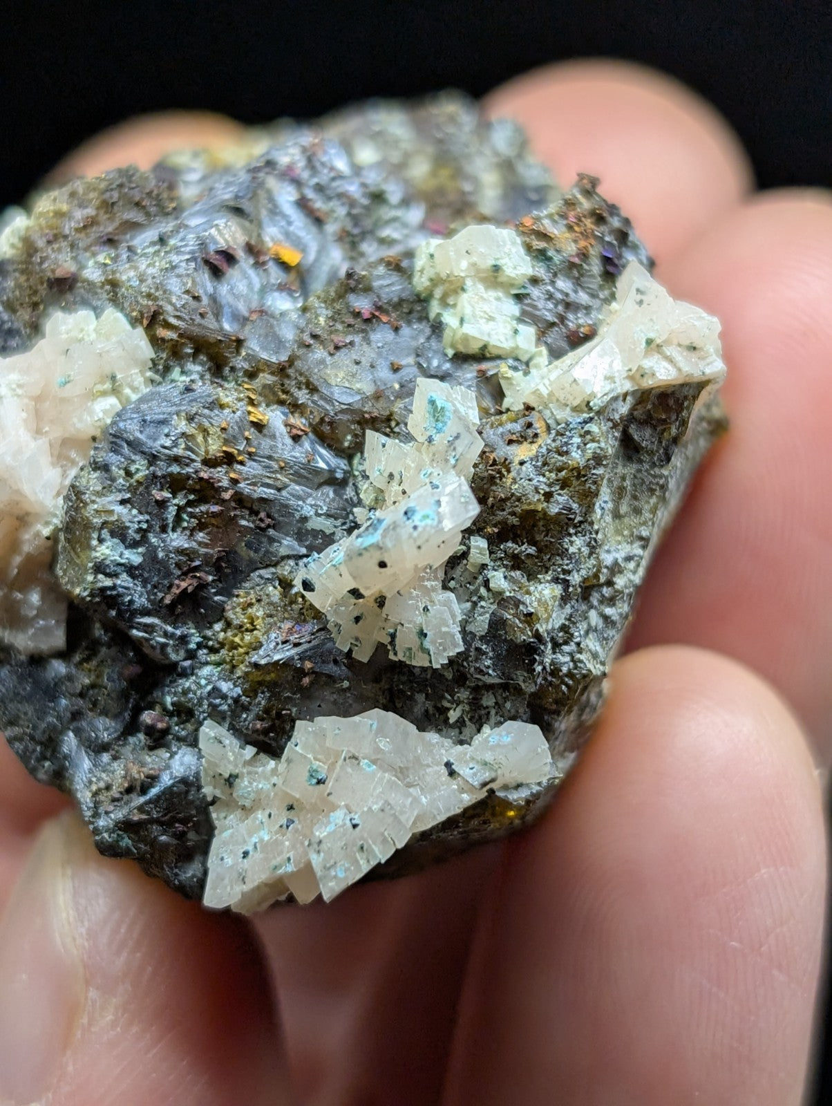 A hand holds a rough, dark gray rock specimen featuring prominent translucent white crystalline formations with subtle blue-green veining.