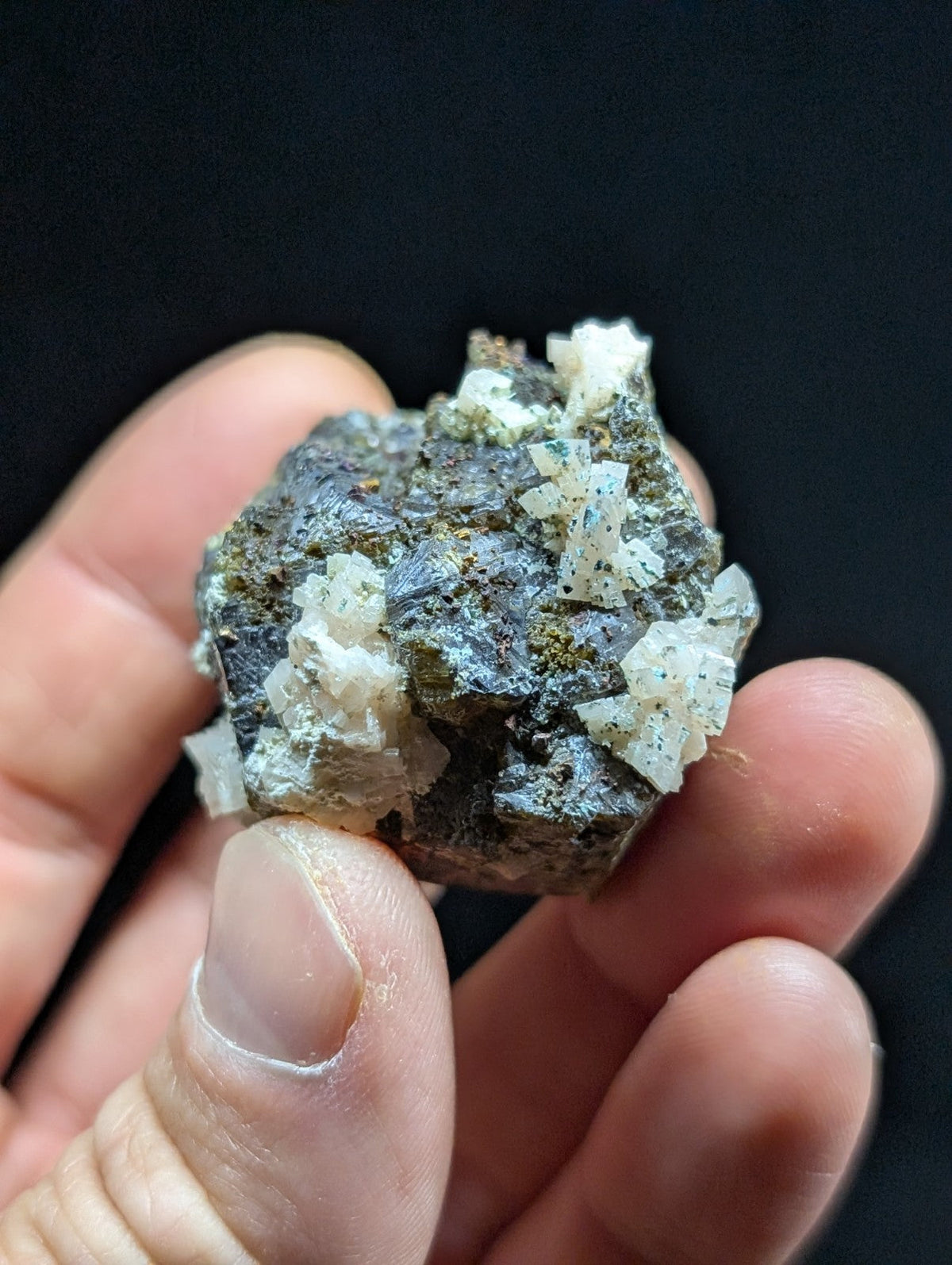 A hand holds a dark gray rock specimen featuring prominent white, crystalline formations with subtle blue flecks.