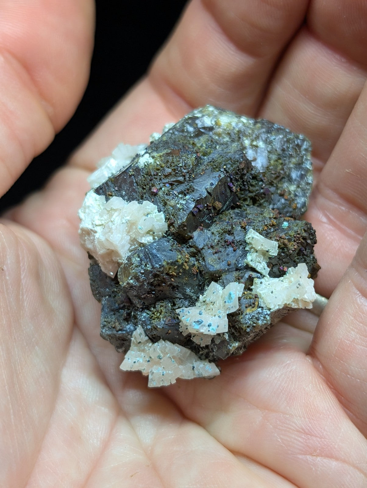 A dark, rough-textured mineral specimen with white crystalline formations and hints of greenish mossy growth.