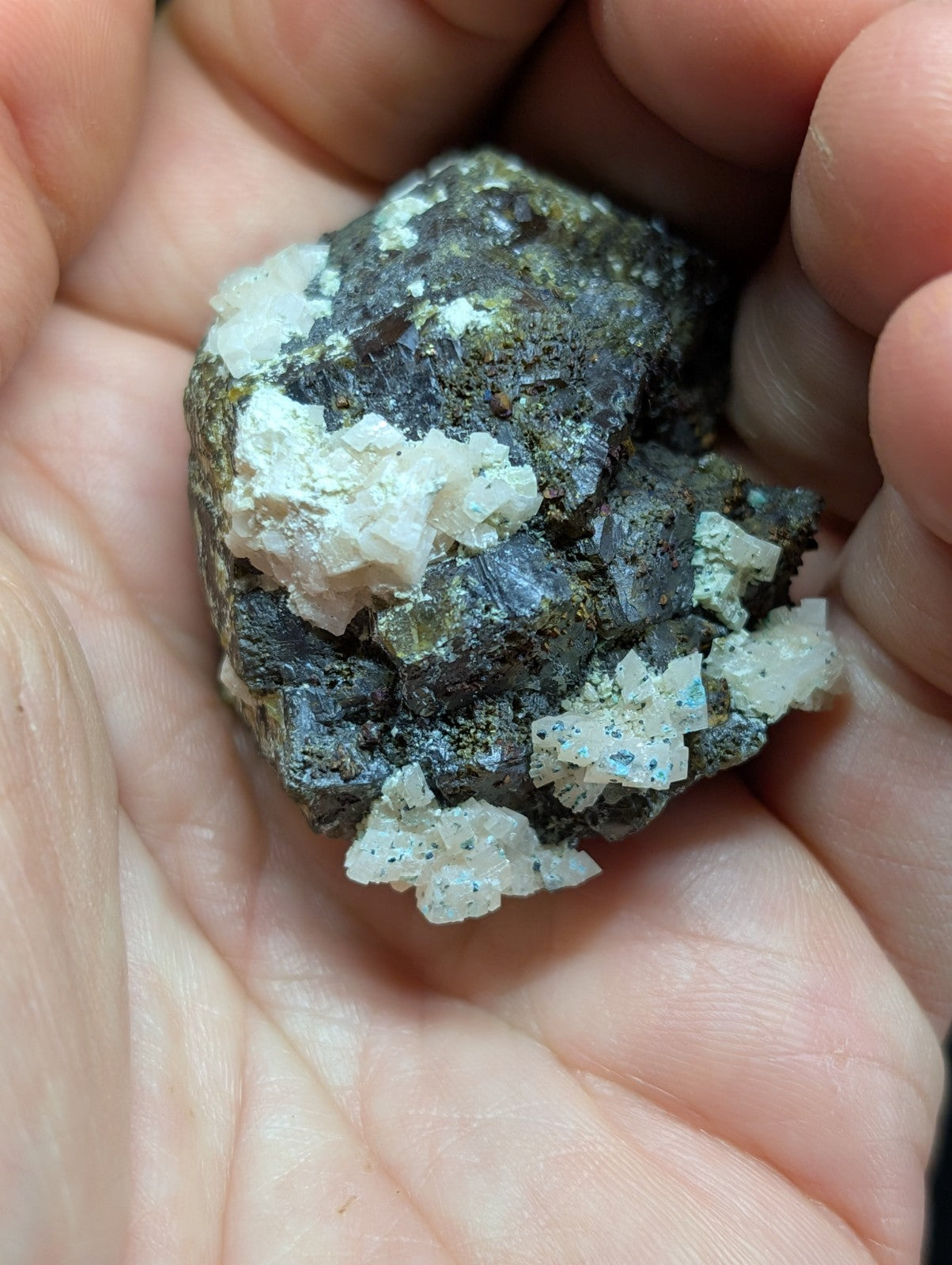 A rough, irregularly shaped mineral specimen featuring a dark matrix with prominent white crystalline formations and subtle blue speckles.