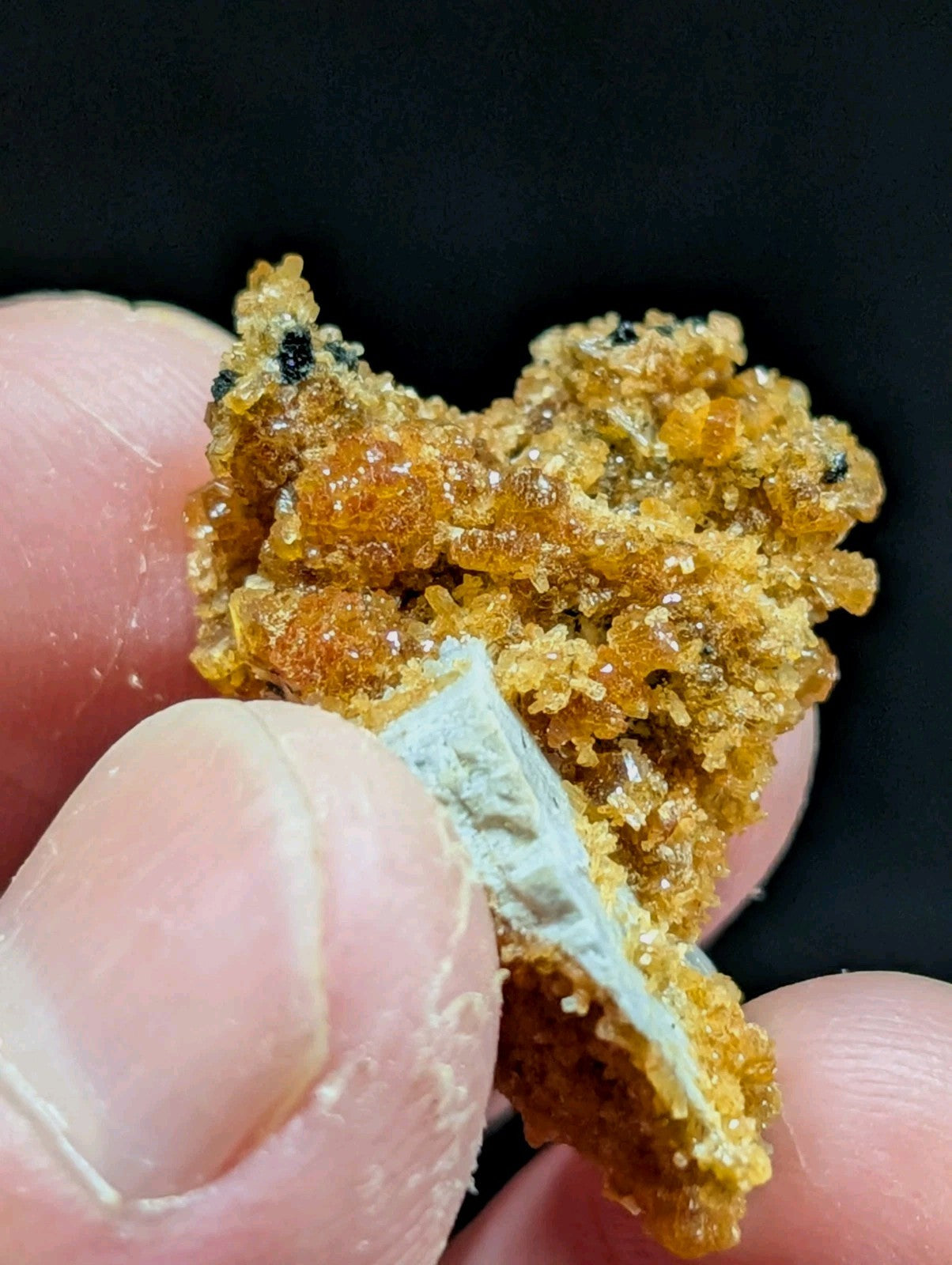 A golden-orange, crystalline rock formation with a rough, sugary texture and small black specks.