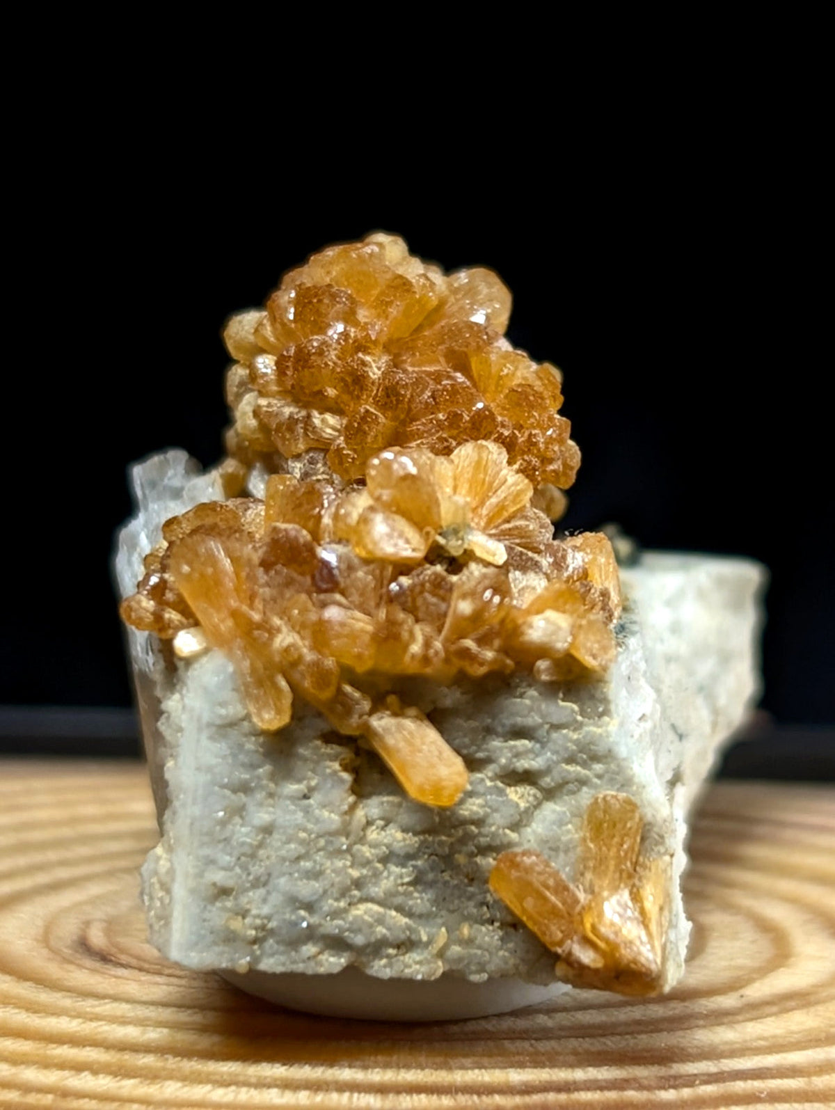 A cluster of translucent amber-colored crystals grows densely atop a rough, light gray rock base.