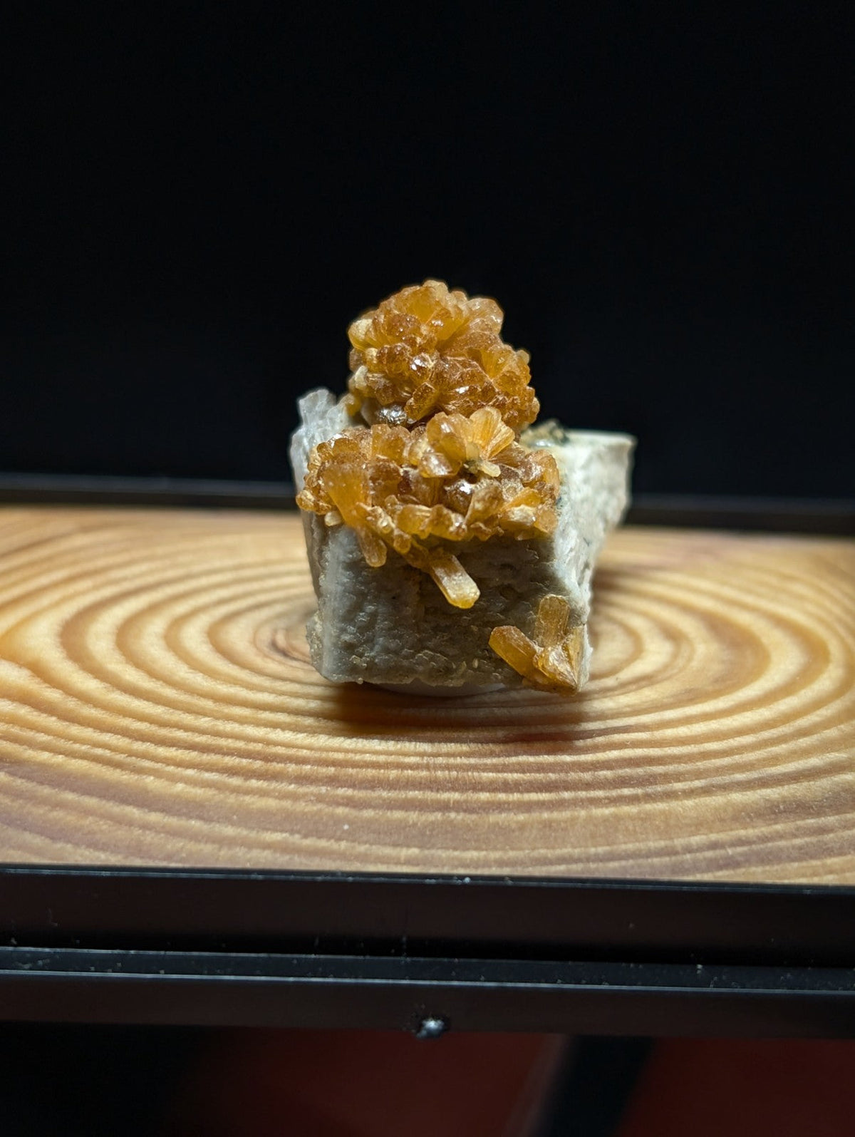 A cluster of golden-orange, crystalline minerals growing atop a gray rock base.