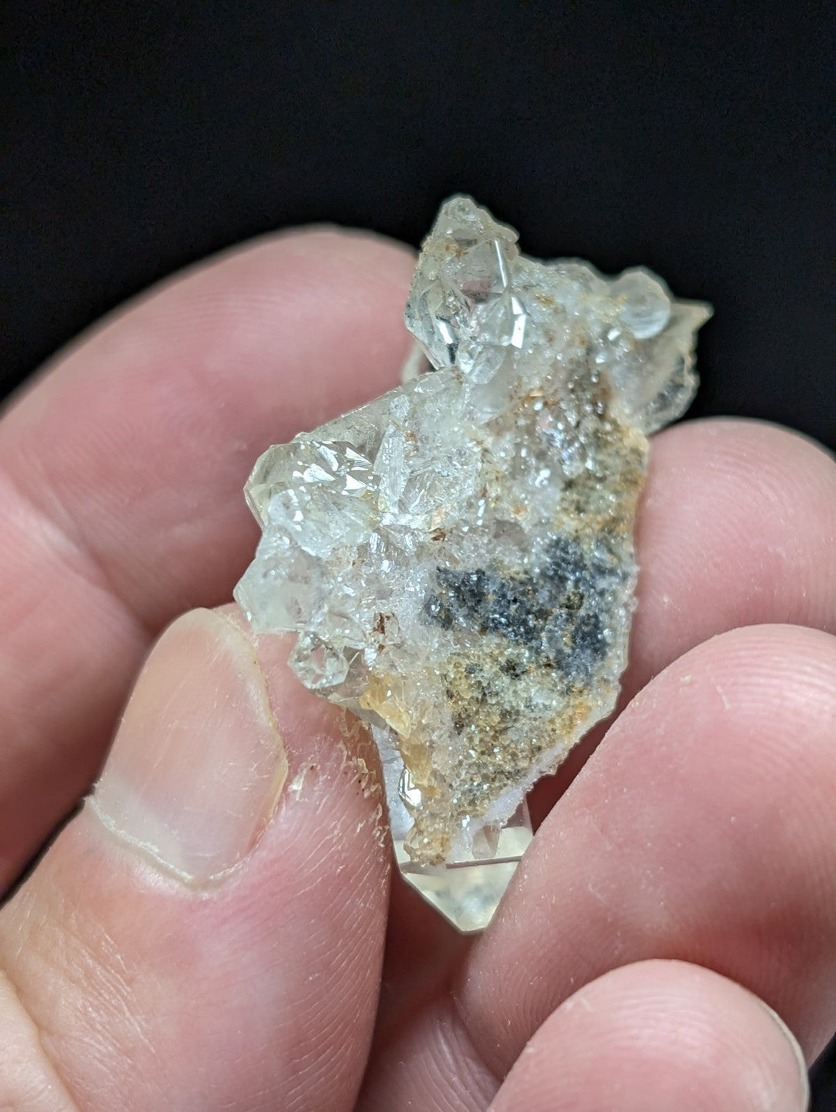 A translucent, crystalline mineral specimen with a rough, jagged surface and patches of dark greenish-black inclusions.