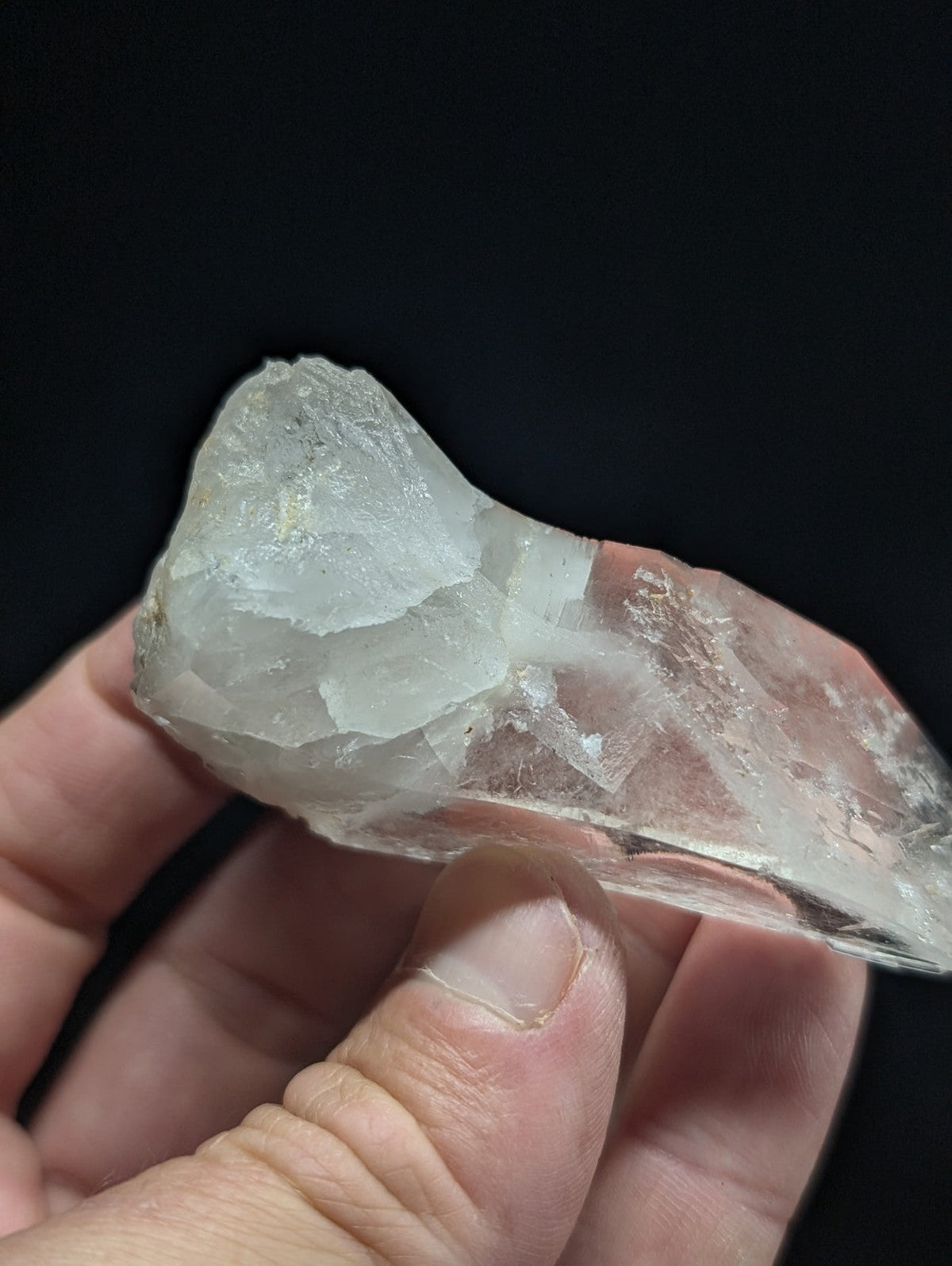 A translucent, pale quartz crystal with a rough, faceted surface and natural striations.