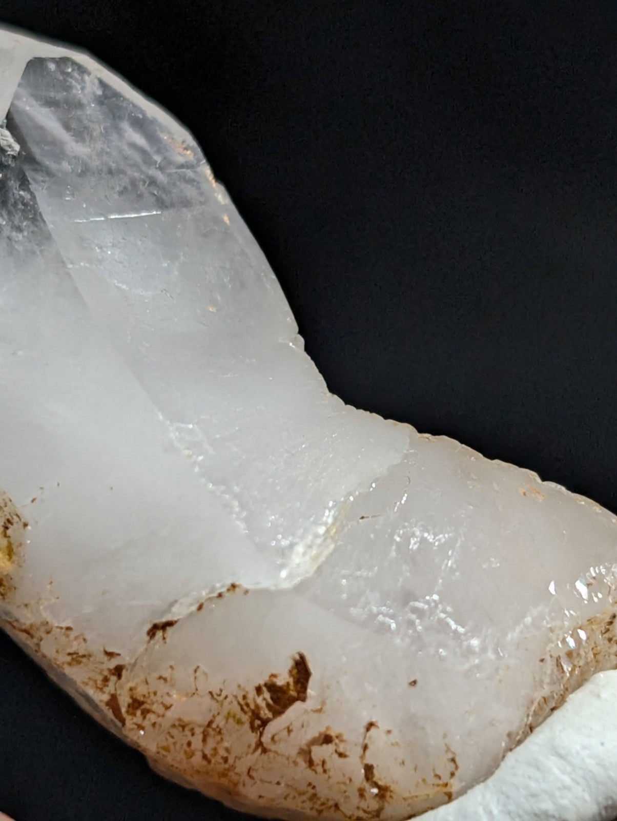 A translucent white quartz crystal with a rough, earthy brown base and natural facets.