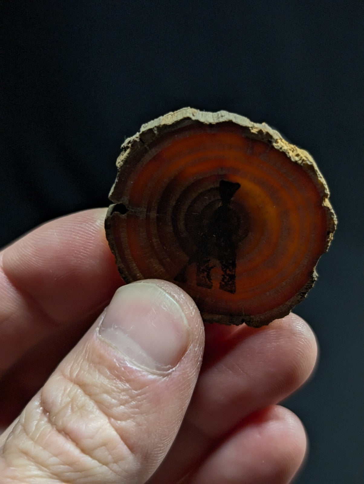 A circular, orange-hued agate slice with concentric rings and a dark silhouette of a figure carved into its center.