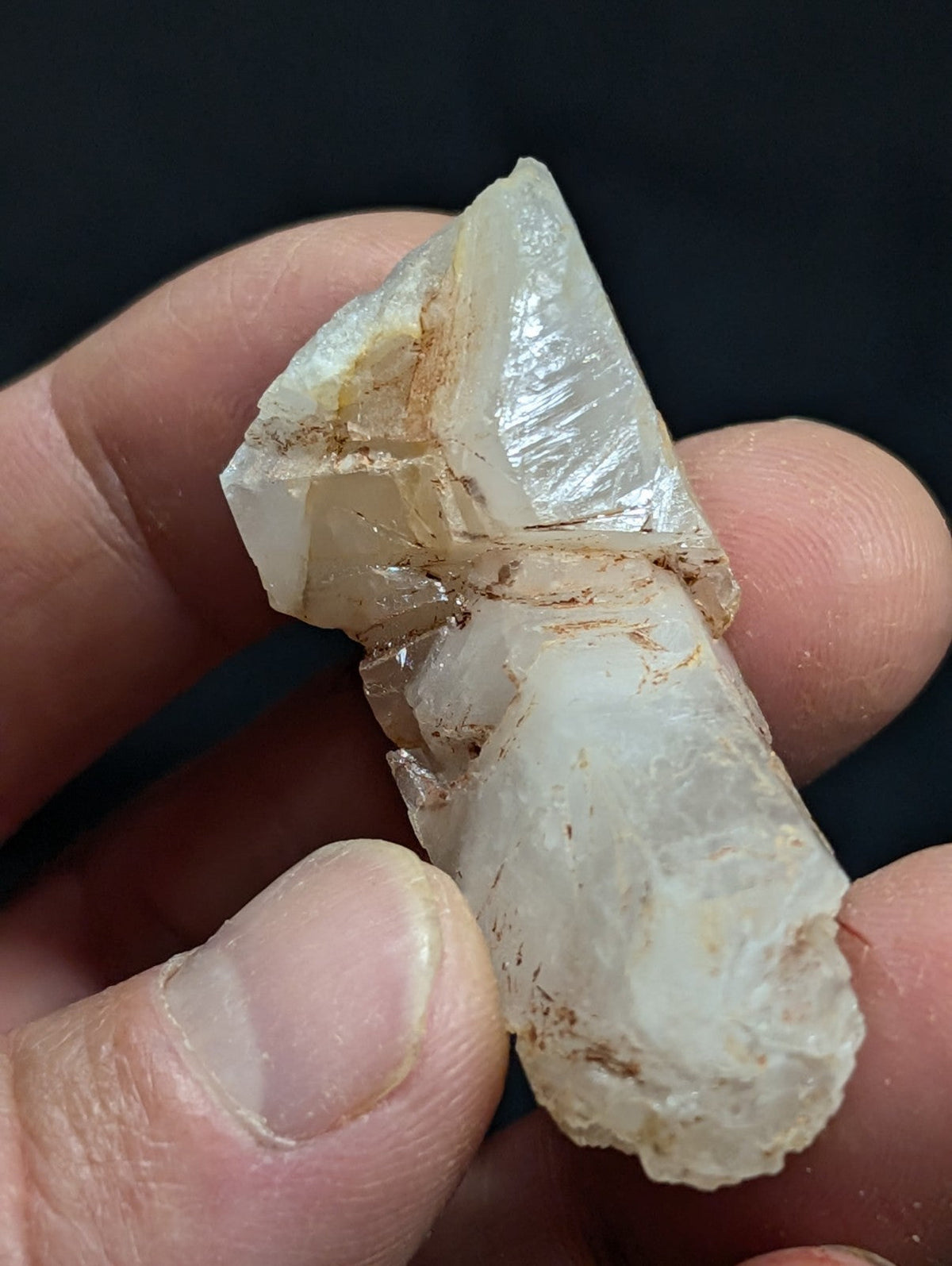 A translucent white quartz crystal with natural facets and brownish mineral inclusions, held gently between fingers.