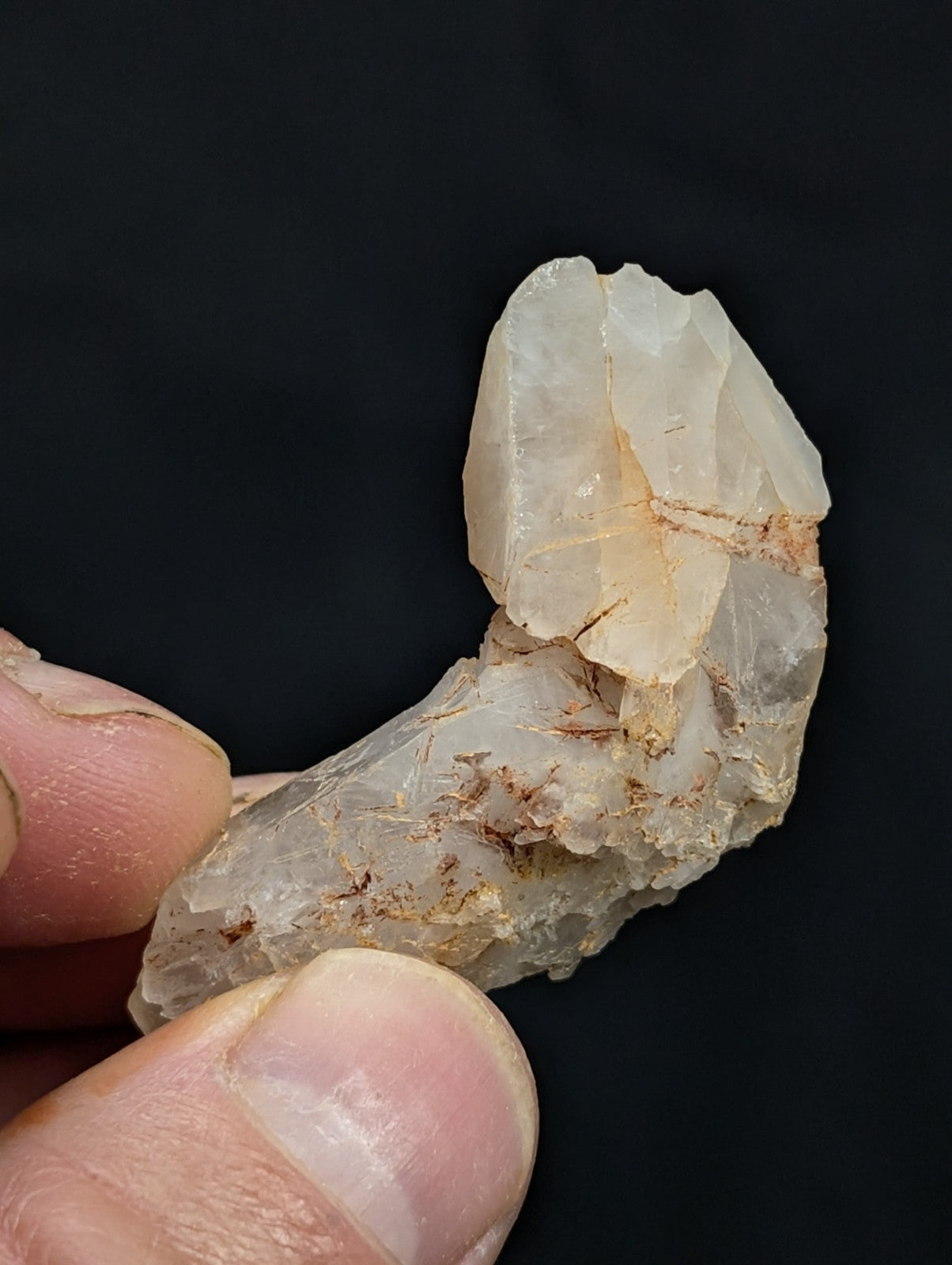 A translucent, pale quartz crystal with natural fractures and earthy brown inclusions.