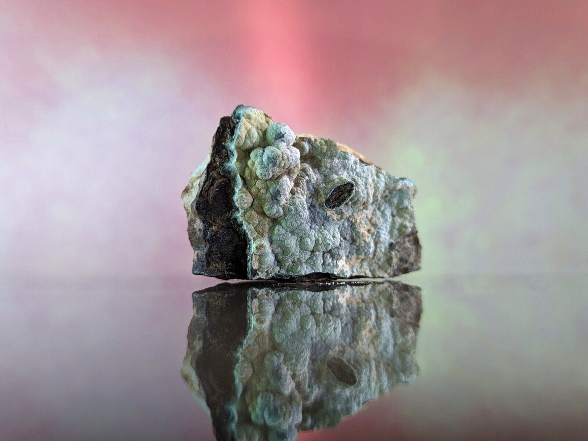 A textured, irregularly shaped mineral specimen with a mix of gray and greenish-blue hues, featuring bumpy, clustered formations on its surface.