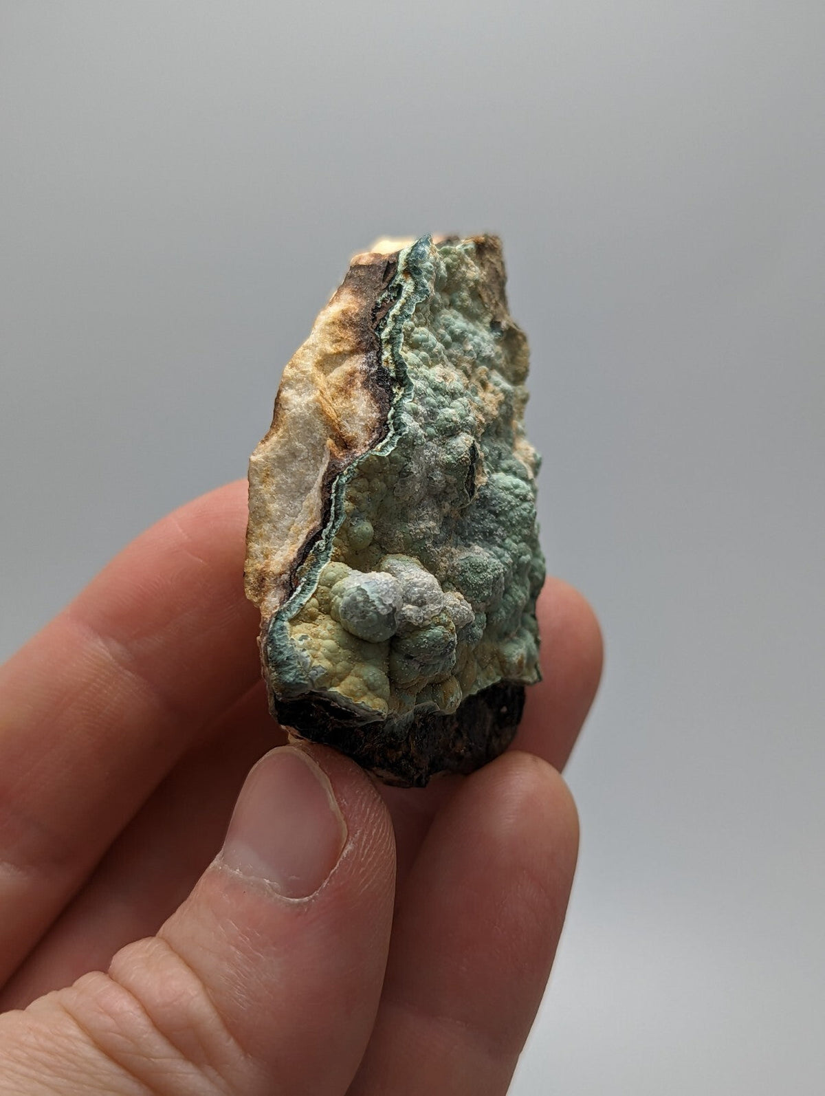 A textured, irregularly shaped mineral specimen with a patchwork of greenish-blue and beige hues, featuring rough, bumpy surfaces.