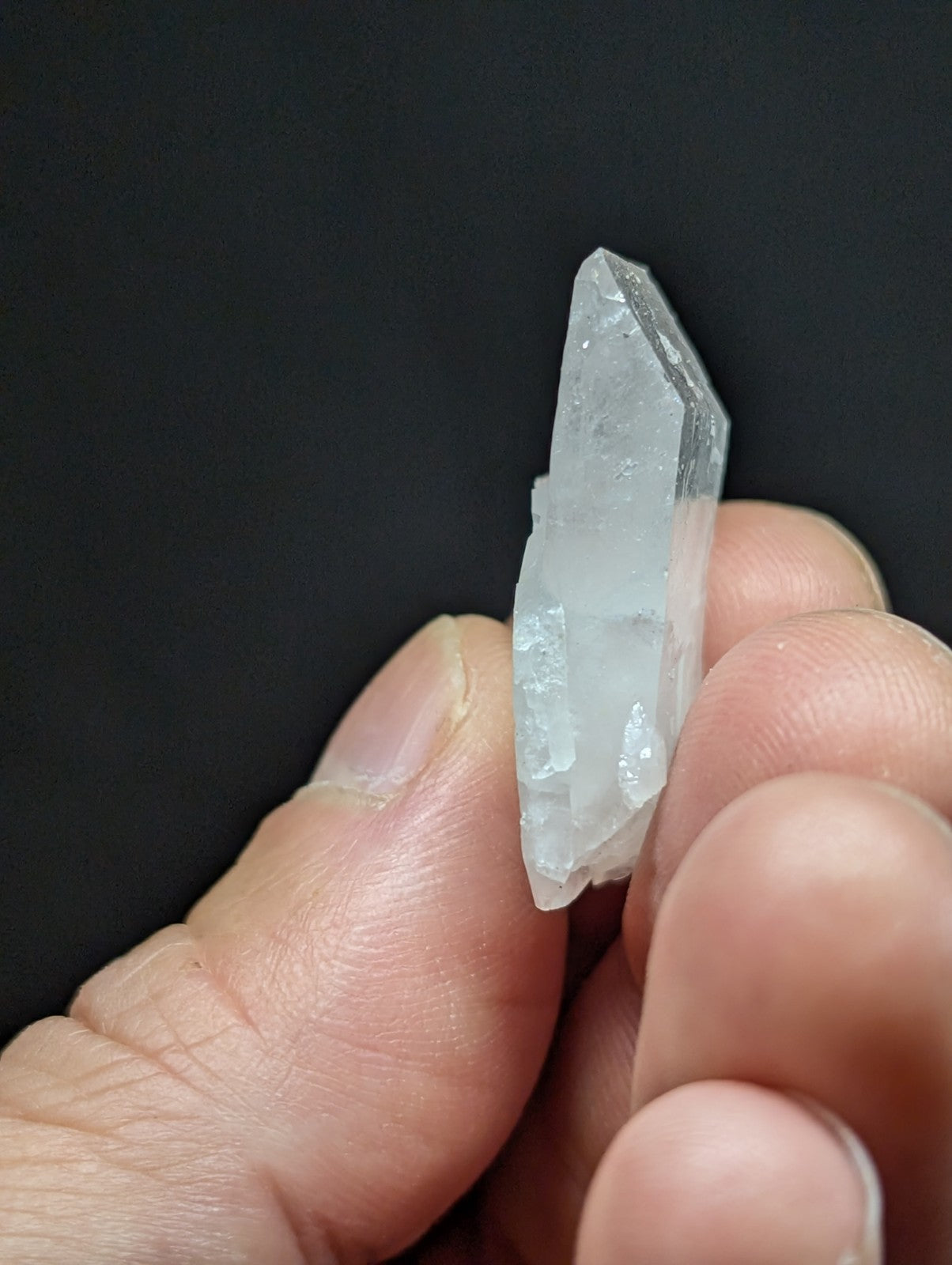 A translucent, clear quartz crystal with a pointed tip and faceted edges.