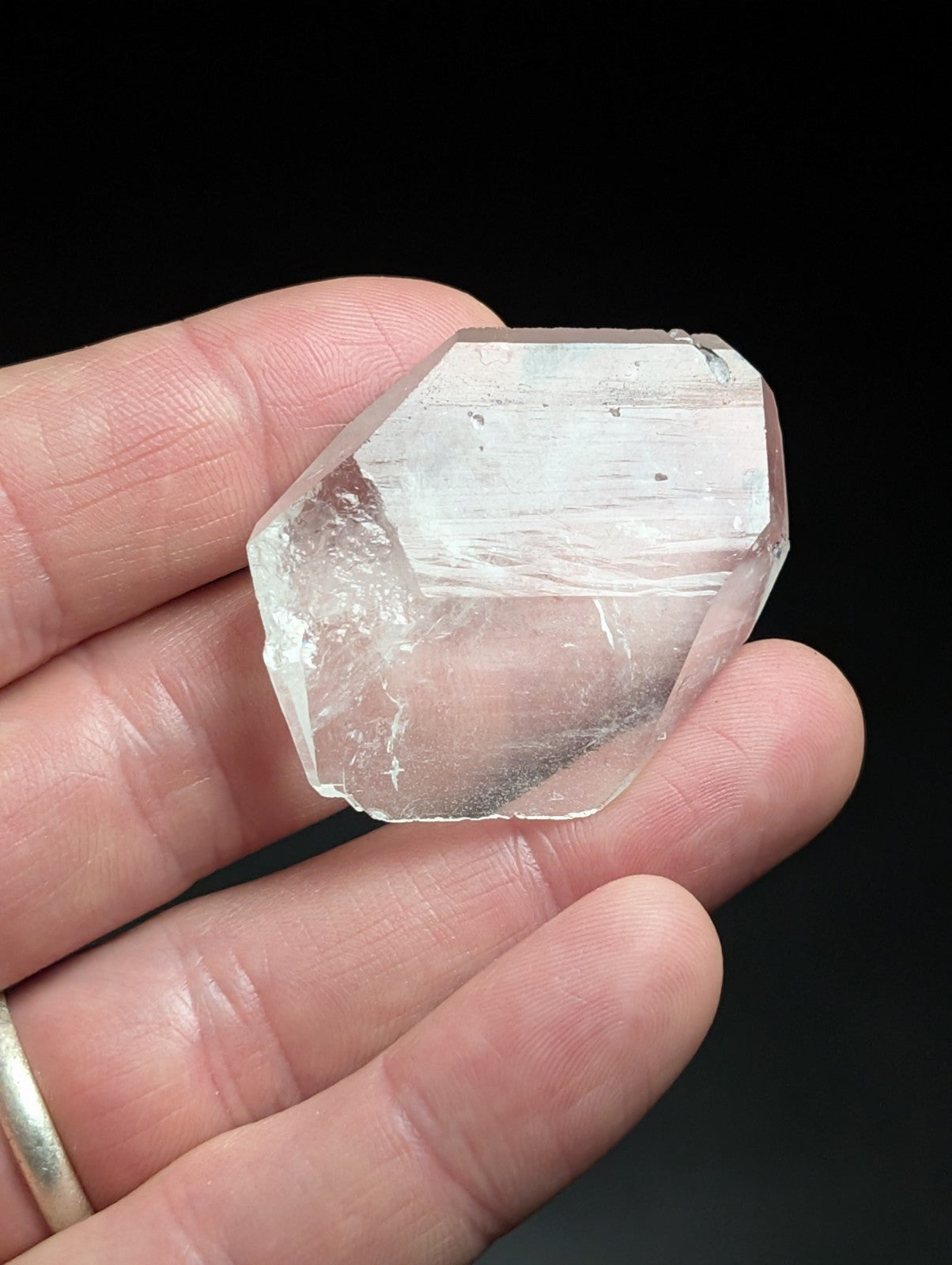 A translucent, hexagonal quartz crystal with subtle internal striations and a slightly pinkish hue.