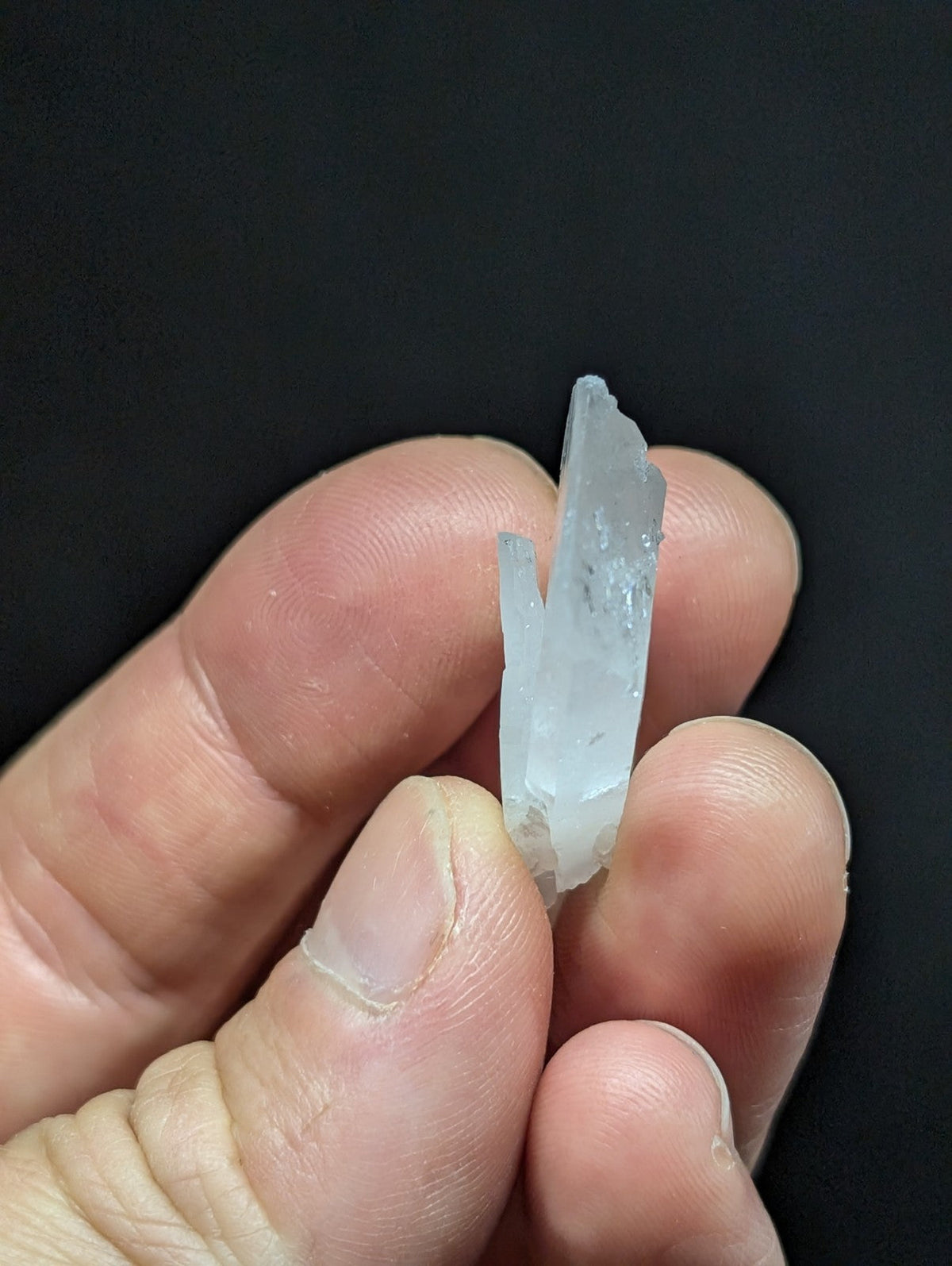 A translucent, pale blue quartz crystal cluster held delicately between fingers.