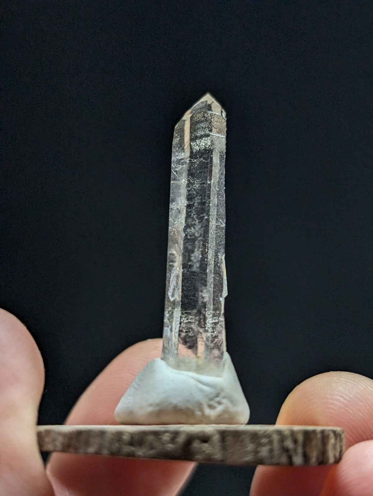 A clear, faceted quartz crystal with a pointed tip and visible internal inclusions is displayed on a small white base.