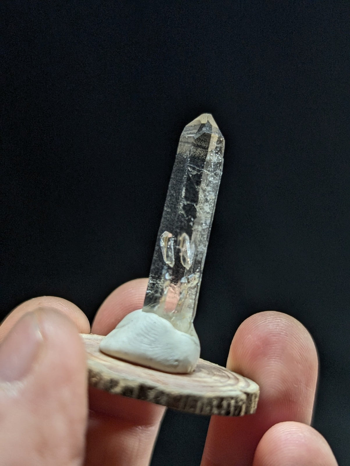A clear, translucent quartz crystal with a pointed tip and natural inclusions sits upright on a small wooden base.