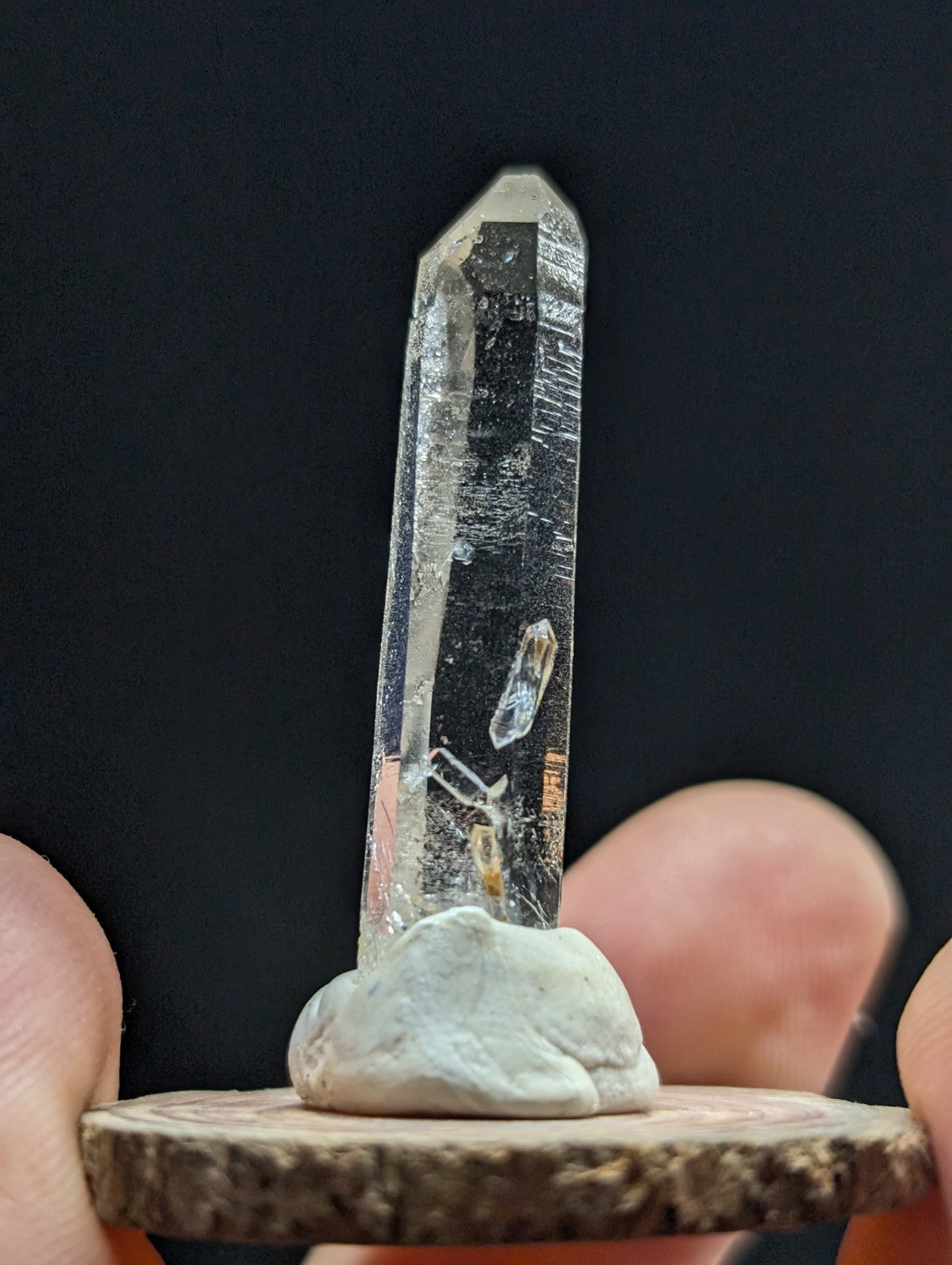 A clear quartz crystal with natural inclusions, mounted on a rustic wooden base.