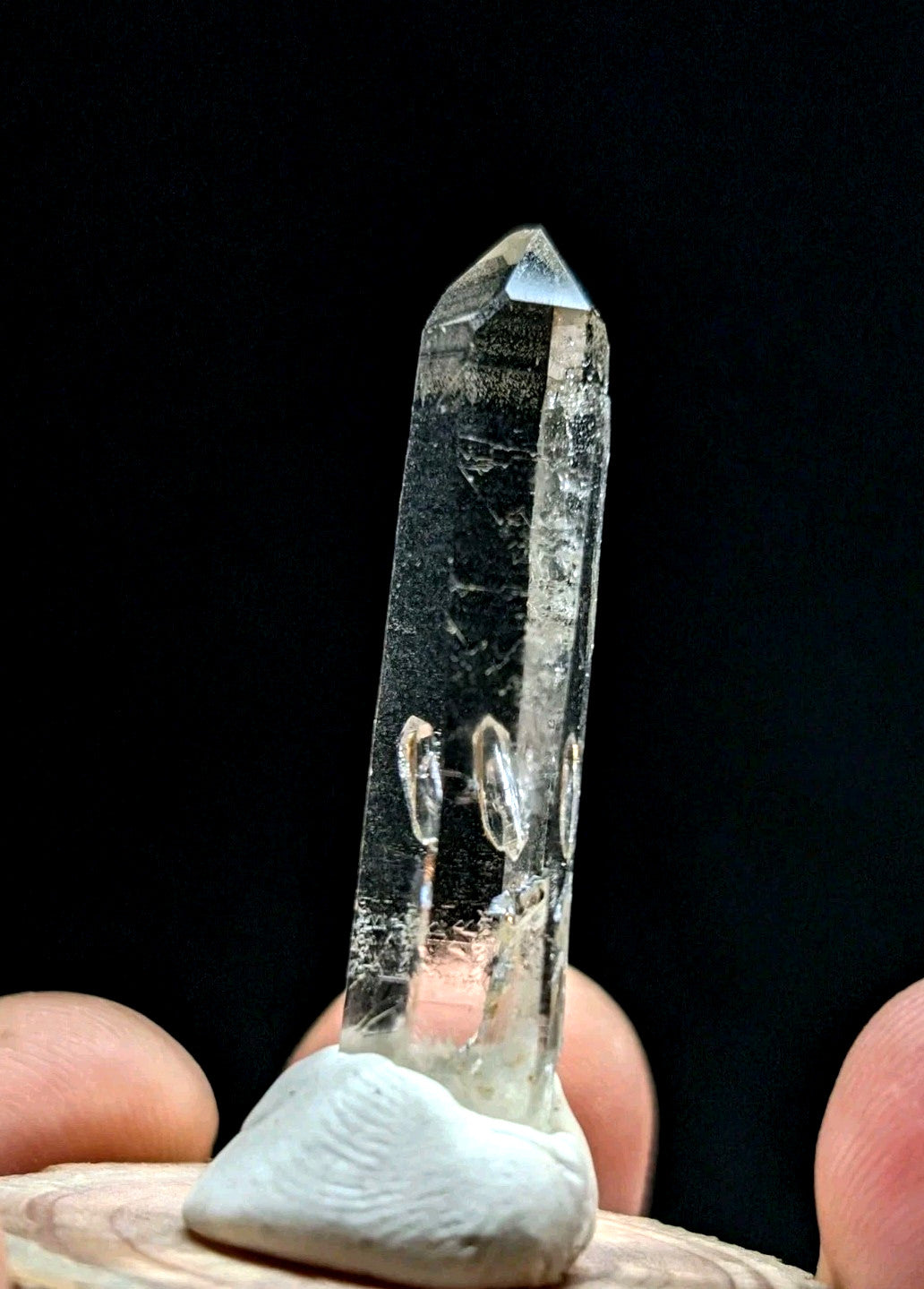 A clear quartz crystal with a pointed tip and natural inclusions, held upright on a white base.