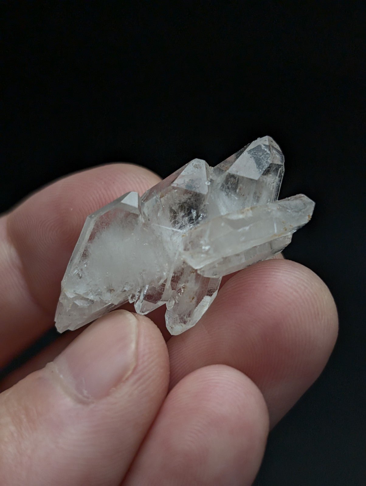 A cluster of clear translucent double terminated floater quartz crystals with sharp facets held in a hand from arkansas