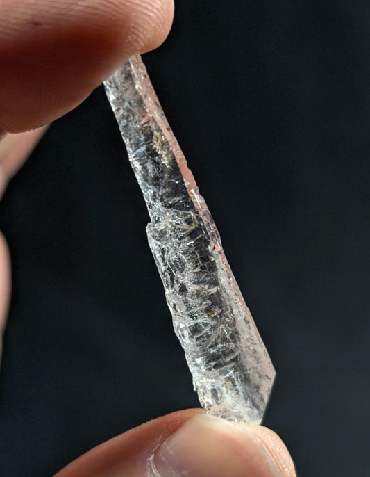 A clear, translucent quartz crystal with a pointed tip and visible internal fractures.