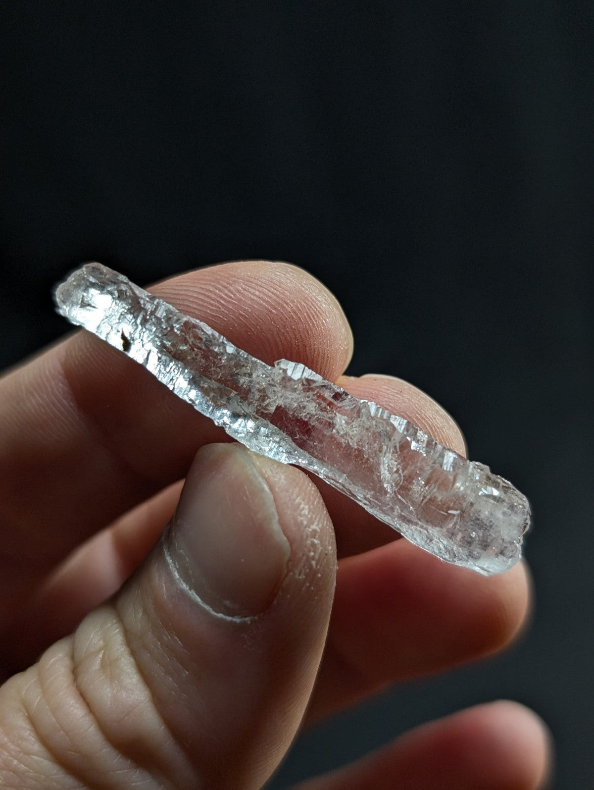 A clear, translucent crystal with jagged edges and a rough, natural texture.
