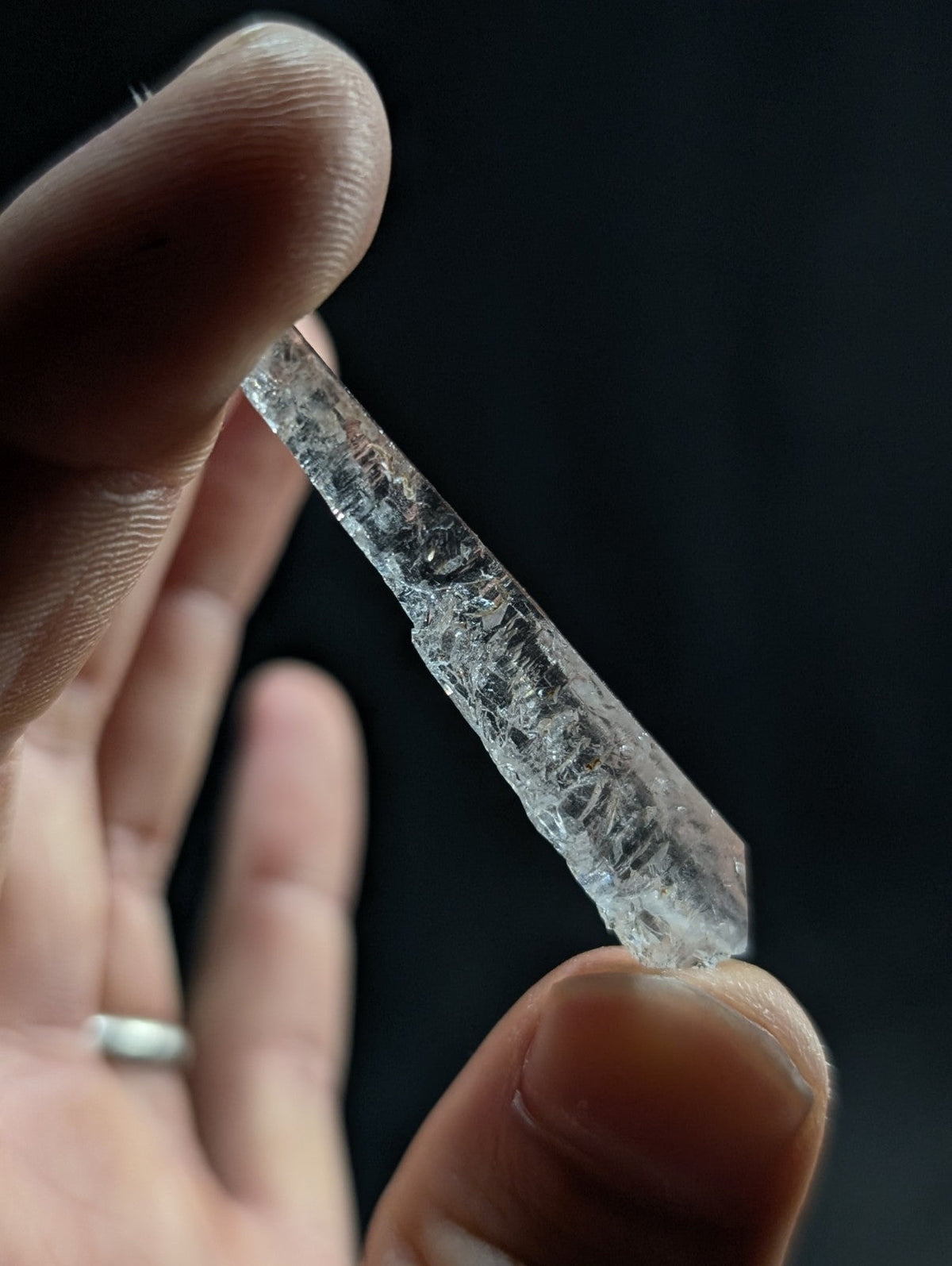 A clear, translucent quartz crystal with a pointed tip and natural facets held between fingers.