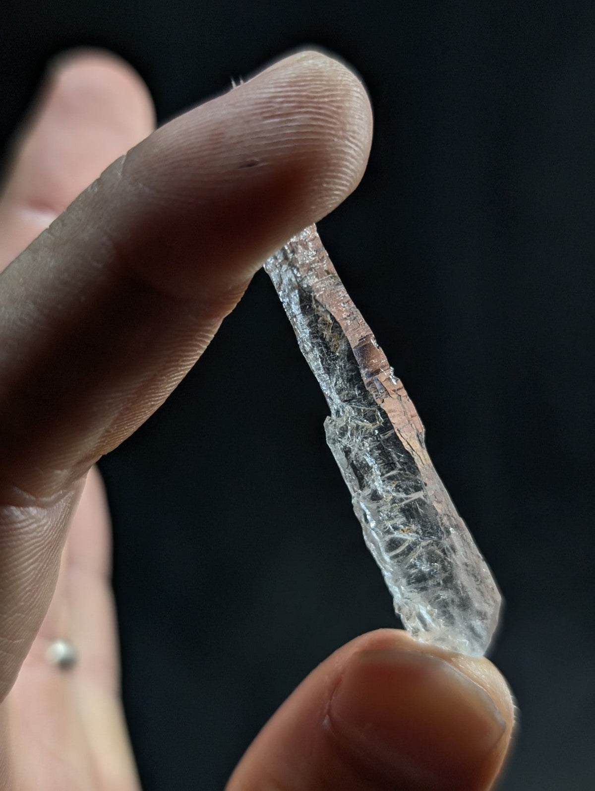 A translucent, clear quartz crystal with natural striations and a rough, jagged edge held between fingers.