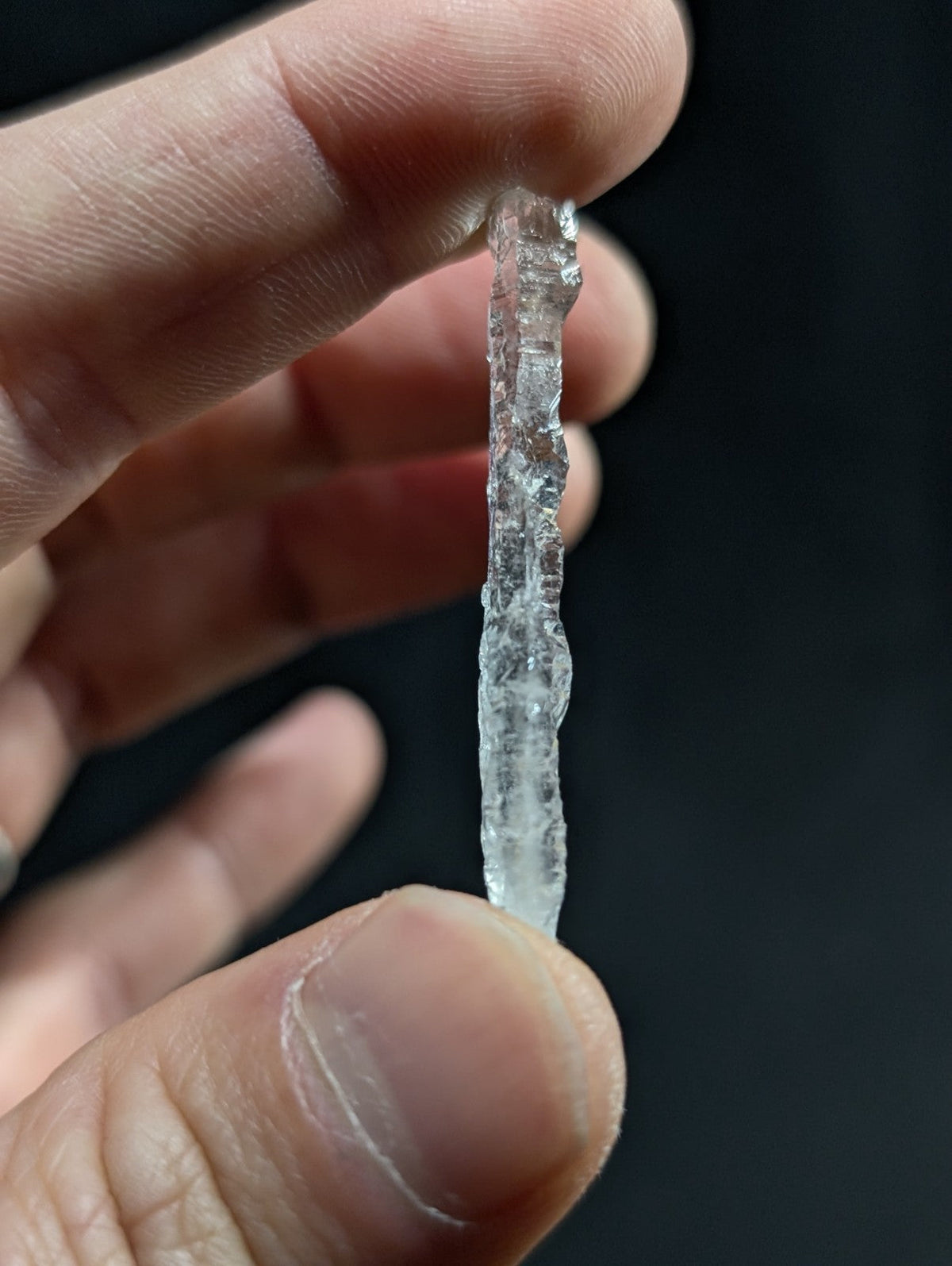 A translucent, irregularly shaped ice stalactite held between fingers.