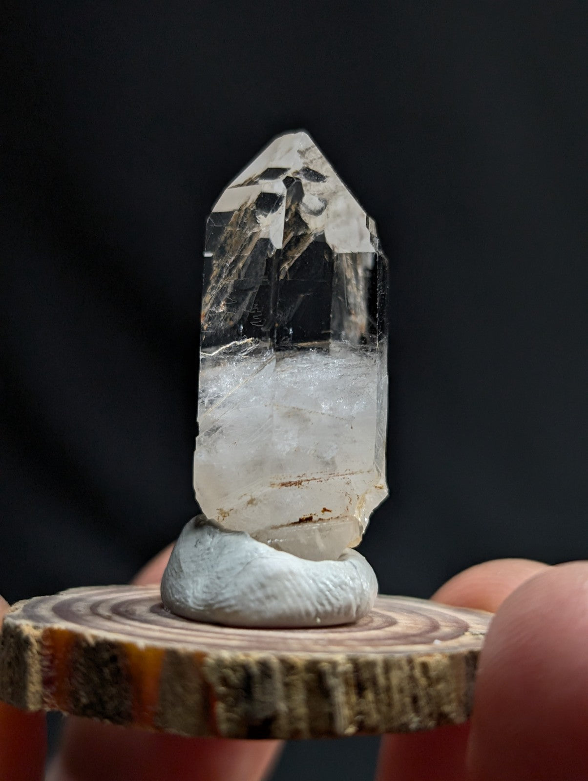 A clear, faceted quartz crystal with a translucent body and subtle internal inclusions sits atop a smooth, light-gray stone base.
