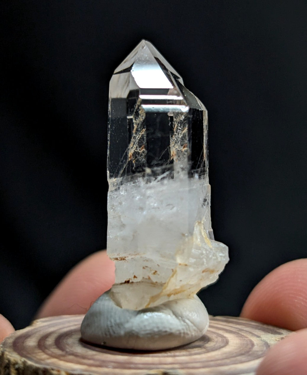 A clear quartz crystal with a pointed top and natural inclusions, mounted on a smooth gray stone base.