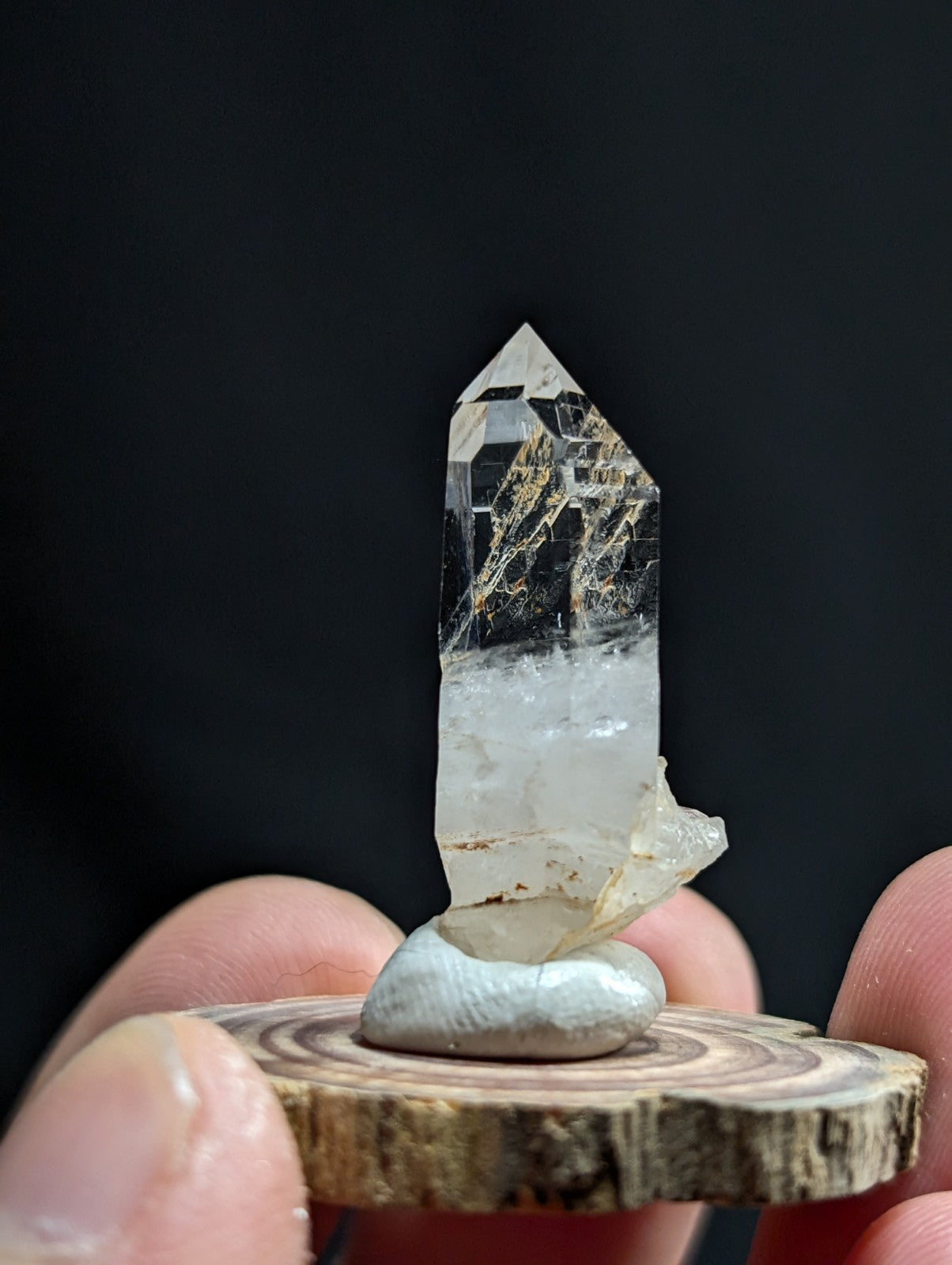 A clear quartz crystal with golden inclusions, standing upright on a smooth white stone base.